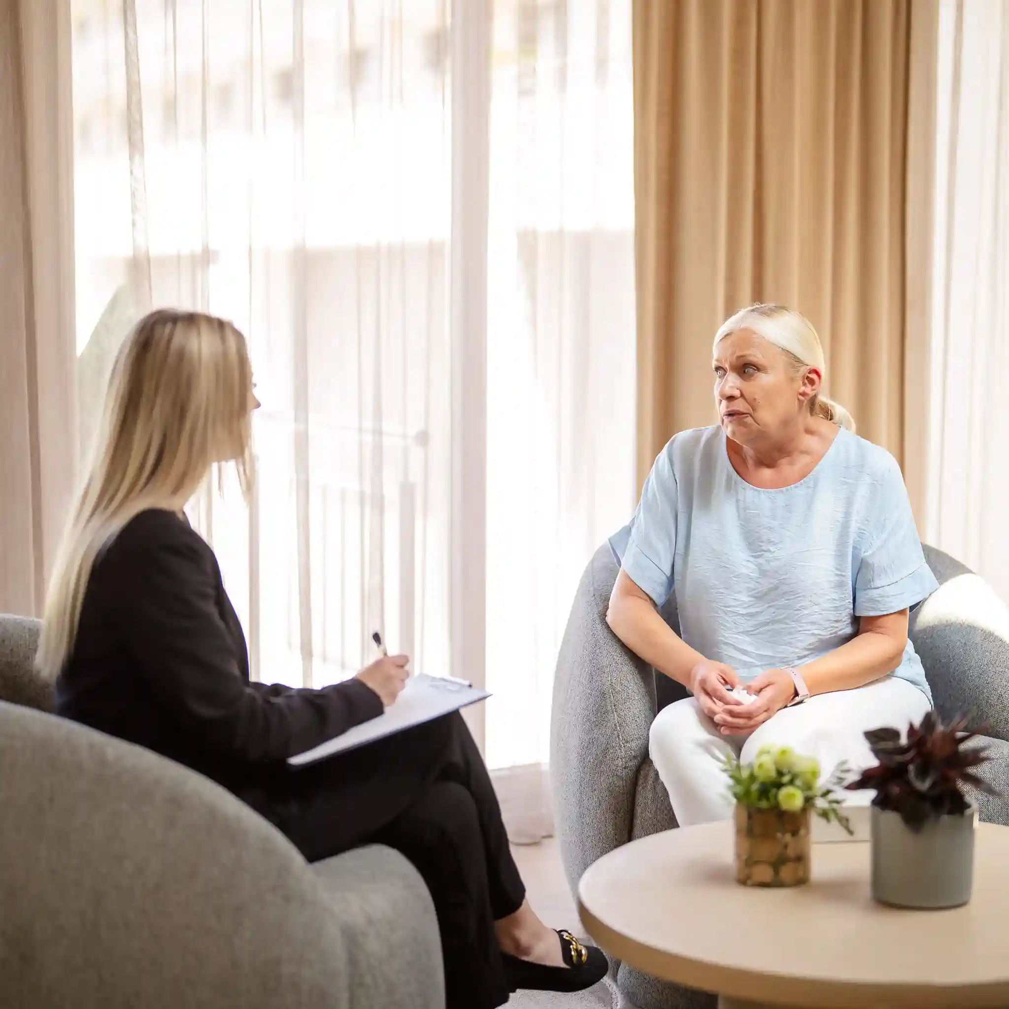 Eine Patientin und eine Psychotherapeutin sitzen sich in Sesseln gegenüber bei einer Therapiestunde.