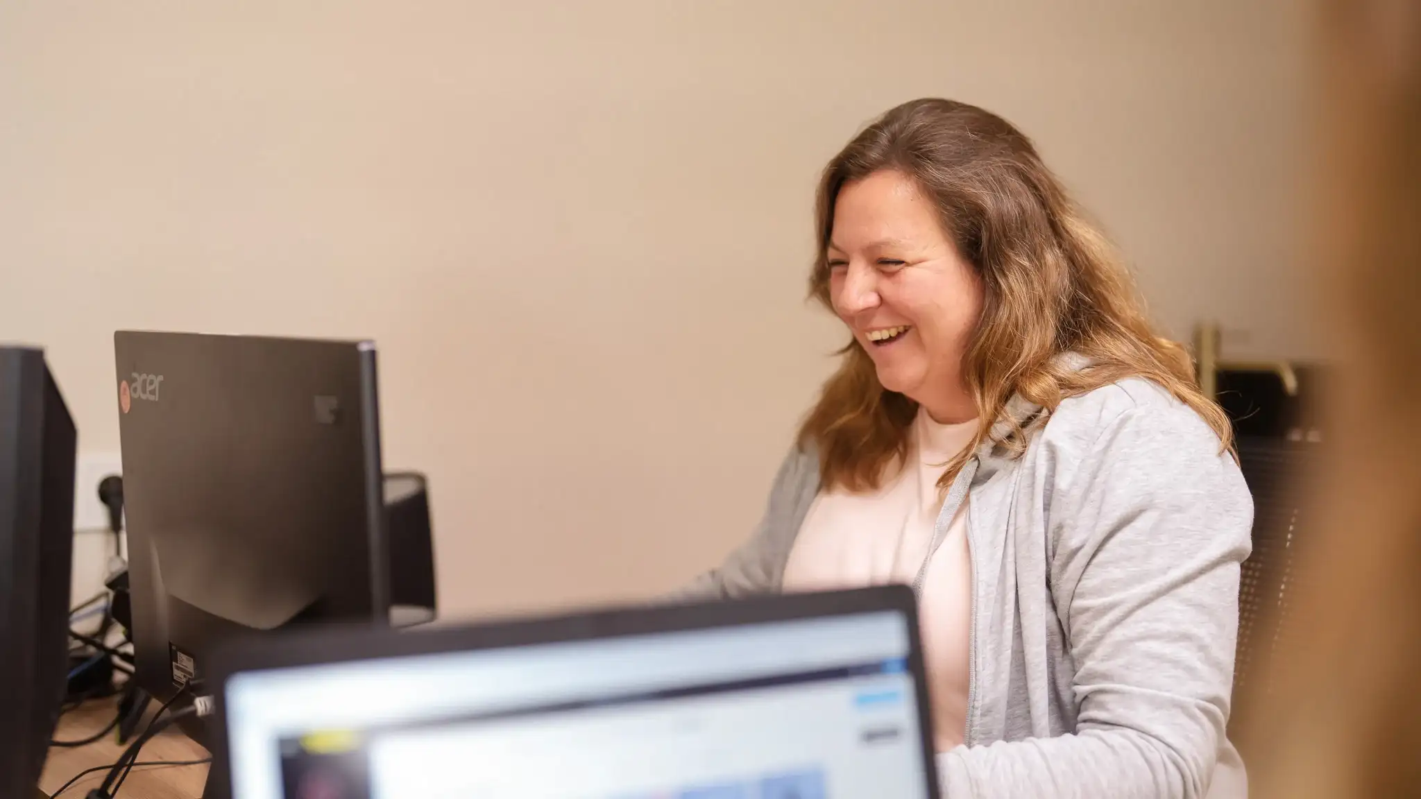 Eine Patientenmanagerin sitzt in einem Büro vor ihrem Computer. Sie ist im Gespräch mit Kolleginnen und lacht.