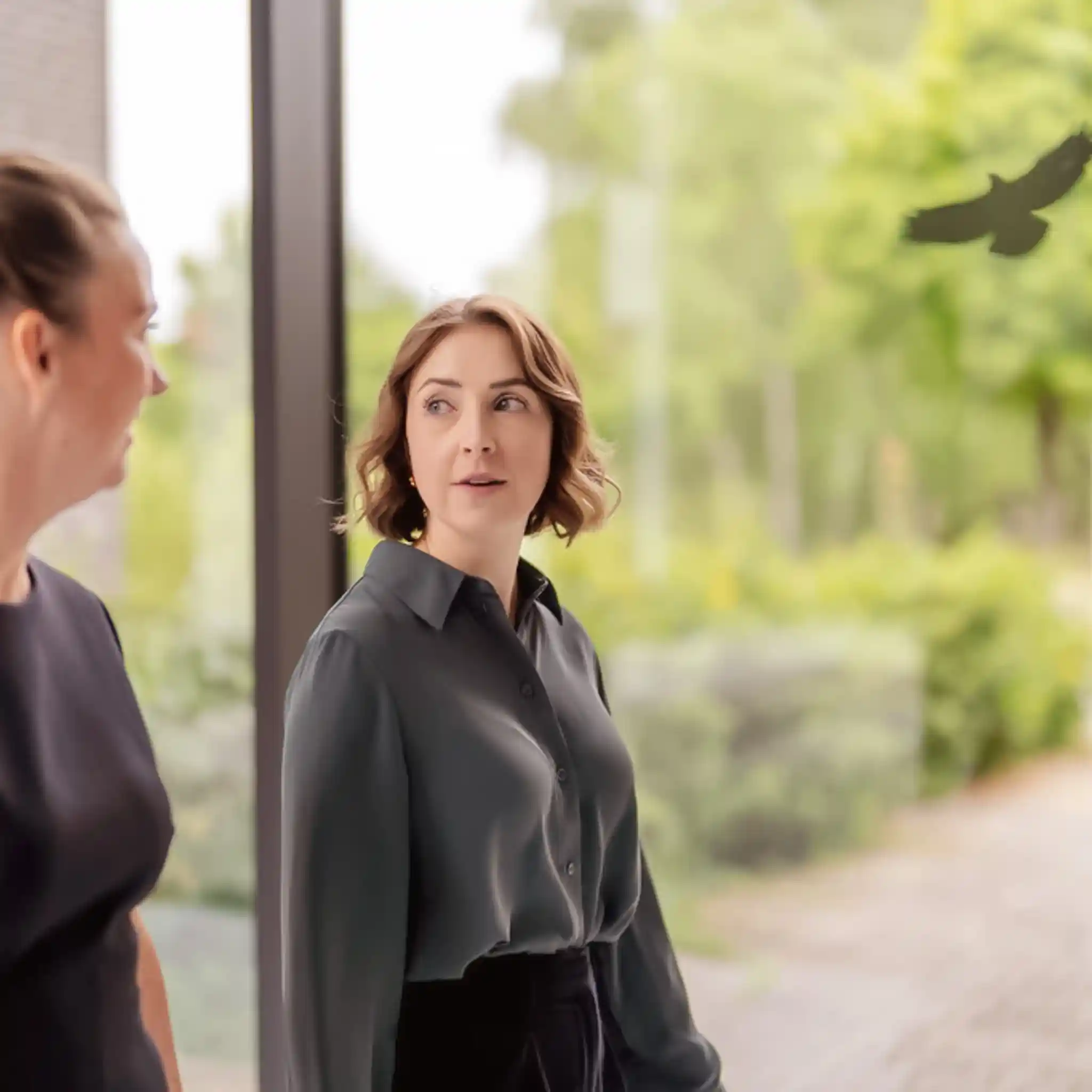 Zwei Frauen laufen vor einem großen Fenster und unterhalten sich