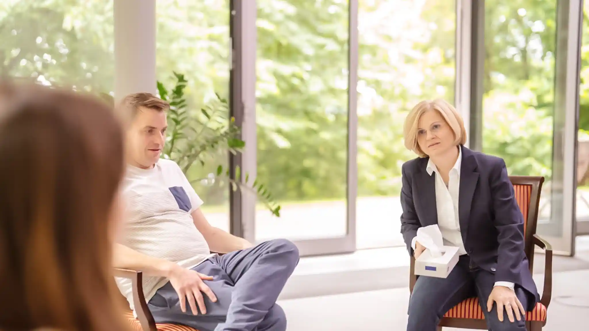 Mehrere Patienten bei der Gruppentherapie. Eine Ärztin hält eine Taschentuchbox.