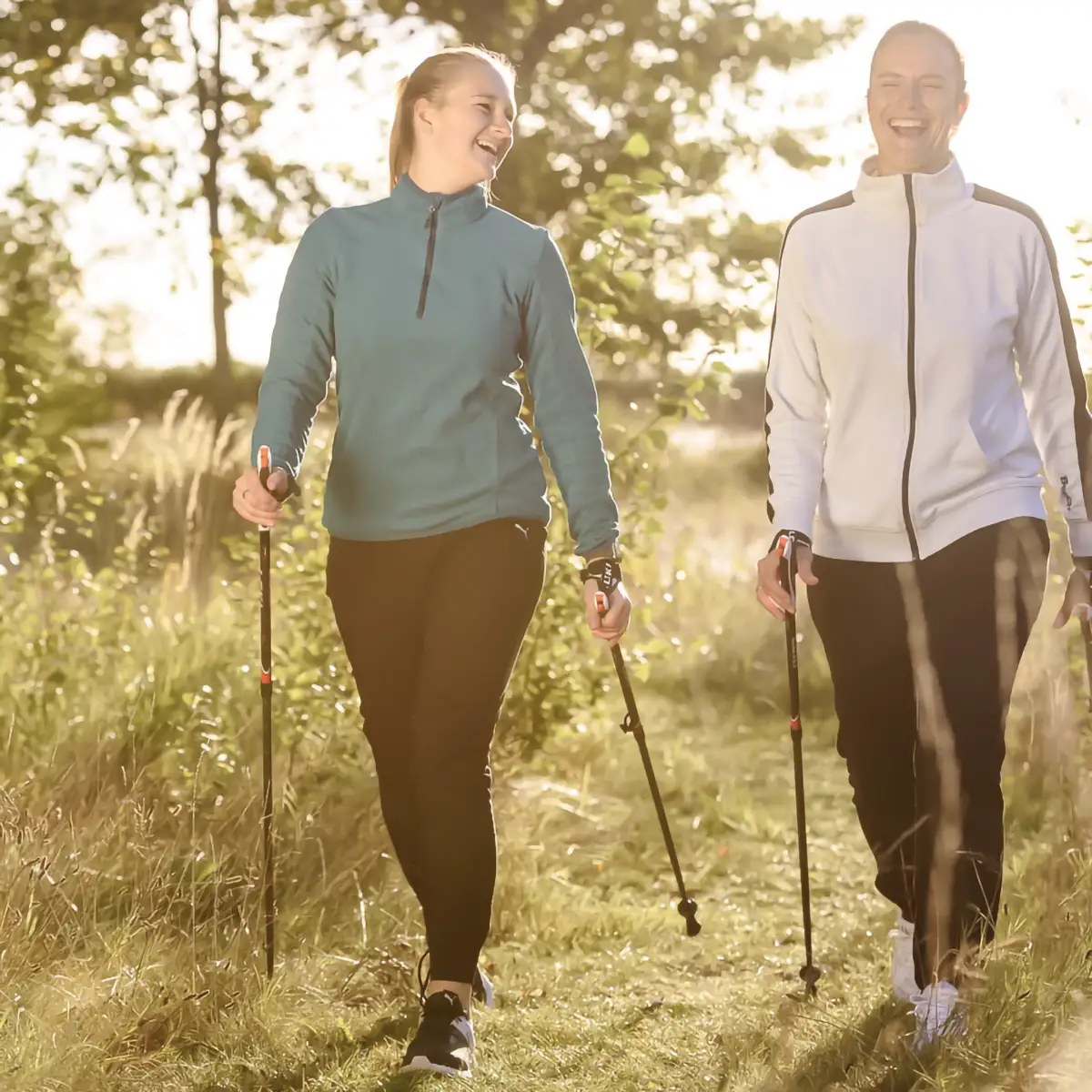 Zwei Frauen laufen mit Nordic-Walking-Stöcken über eine Wiese