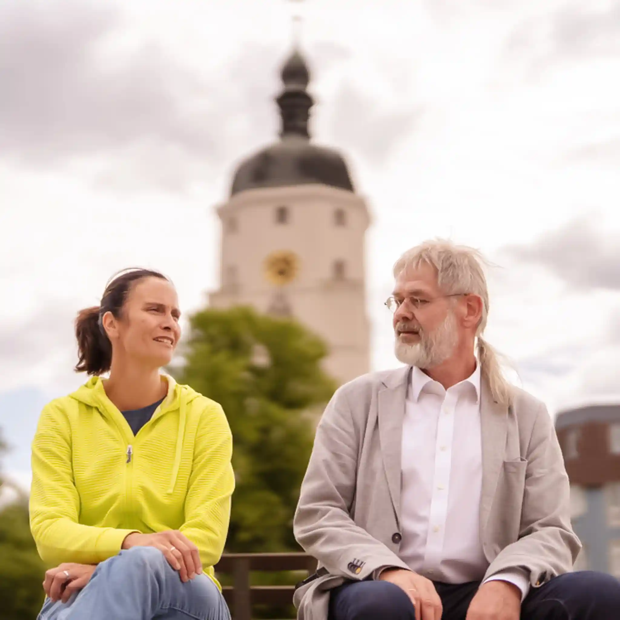 Eine Patientin und ihr Arzt sitzen nebeneinander auf einer Parkbank.