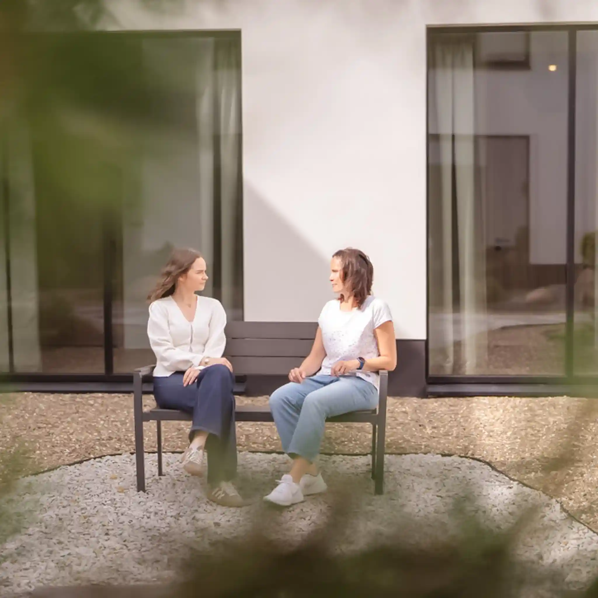 Zwei Patientinnen sitzen zusammen auf einer Bank und unterhalten sich.