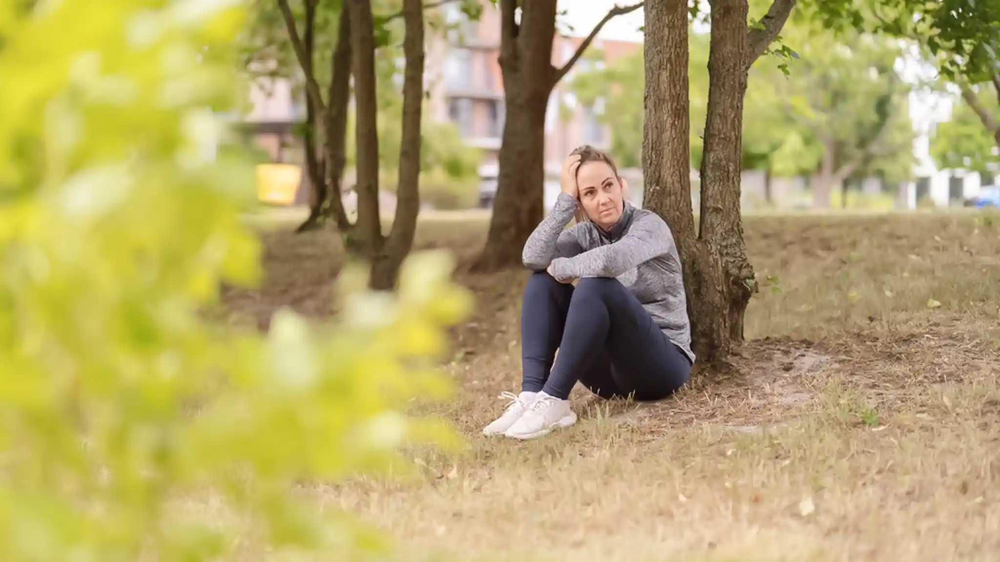 Eine Frau sitzt an einen Baum gelehnt auf dem Boden