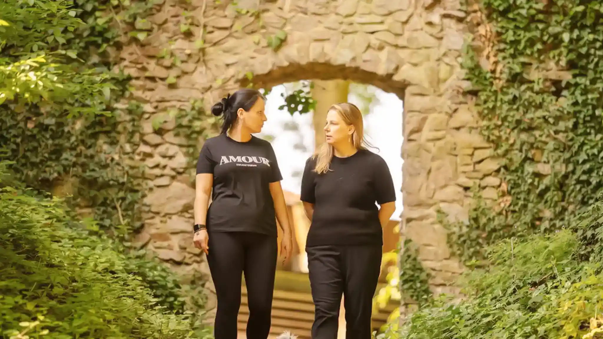 Zwei Frauen laufen nebeneinander her durch einen Innenhof und unterhalten sich.