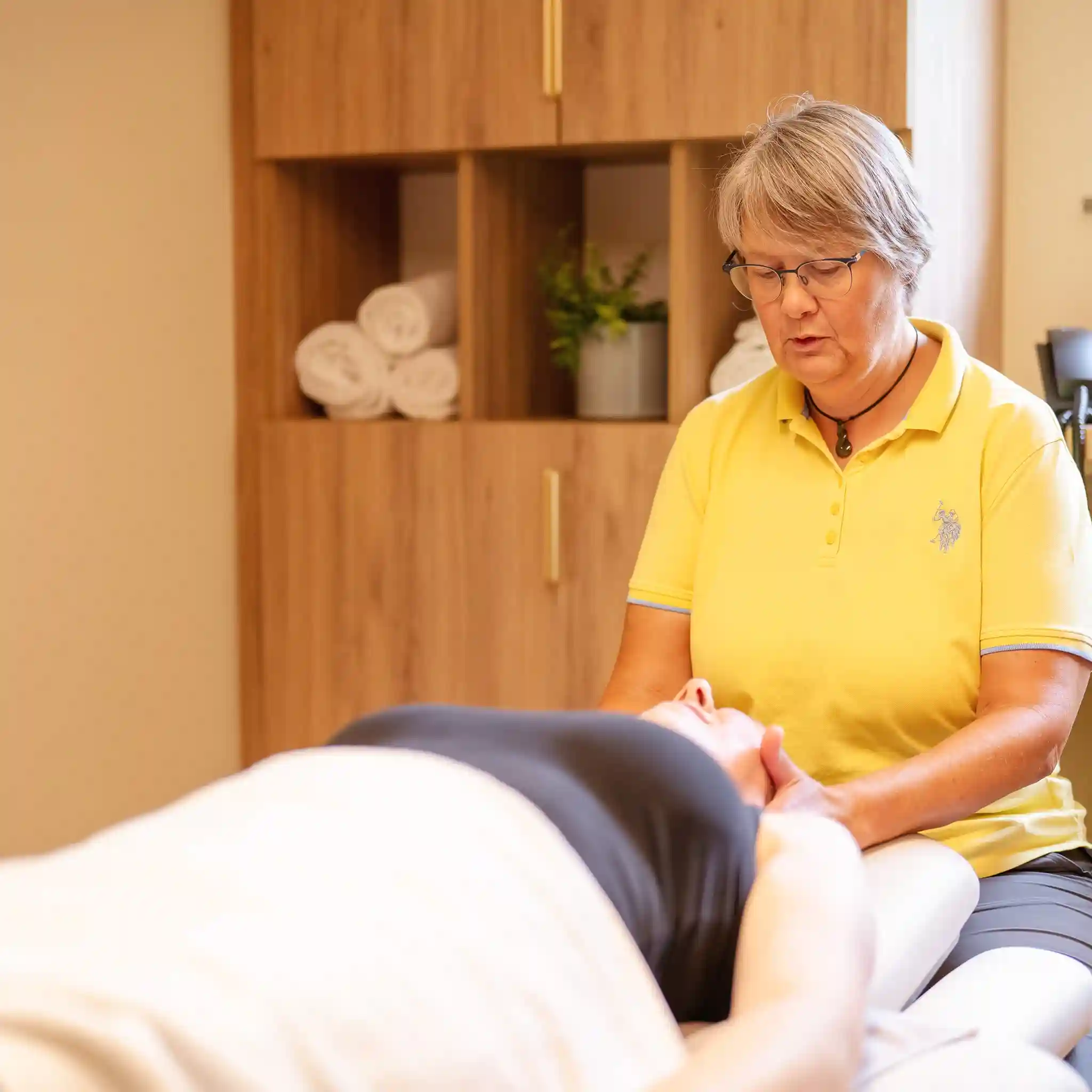 Eine Physiotherapeutin führt eine Fango-Nackenmassage bei einem Patienten durch.