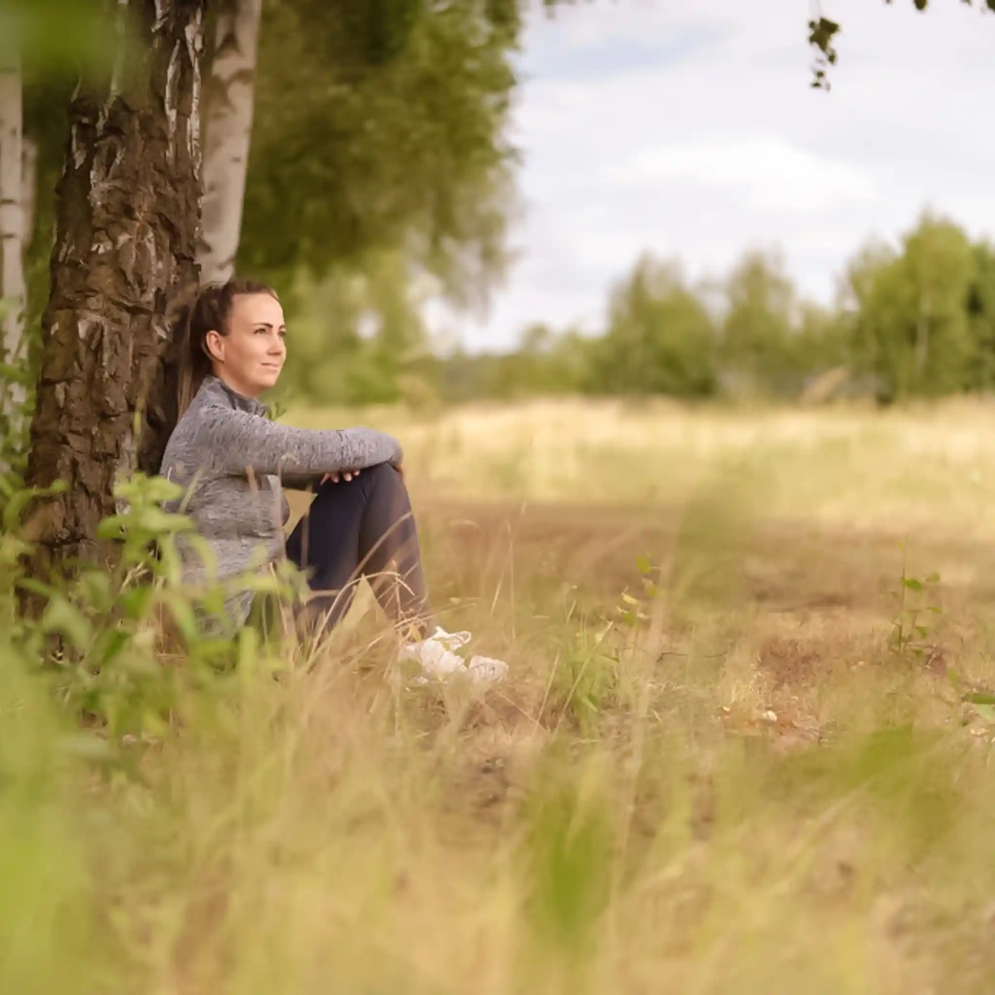 Eine Frau sitzt nachdenklich an einem Baum auf einer Wiese