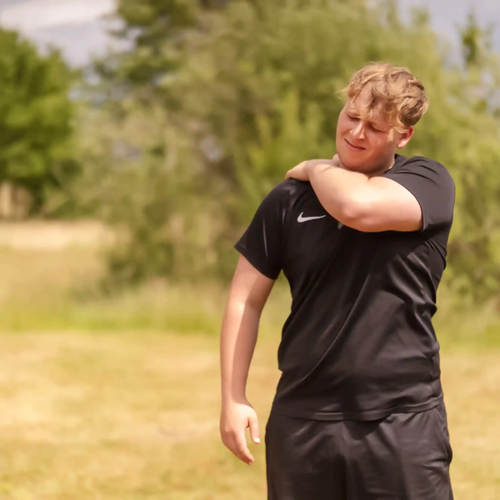 Ein Patient steht auf einer Wiese und hält sich den Rücken mit schmerzendem Gesicht
