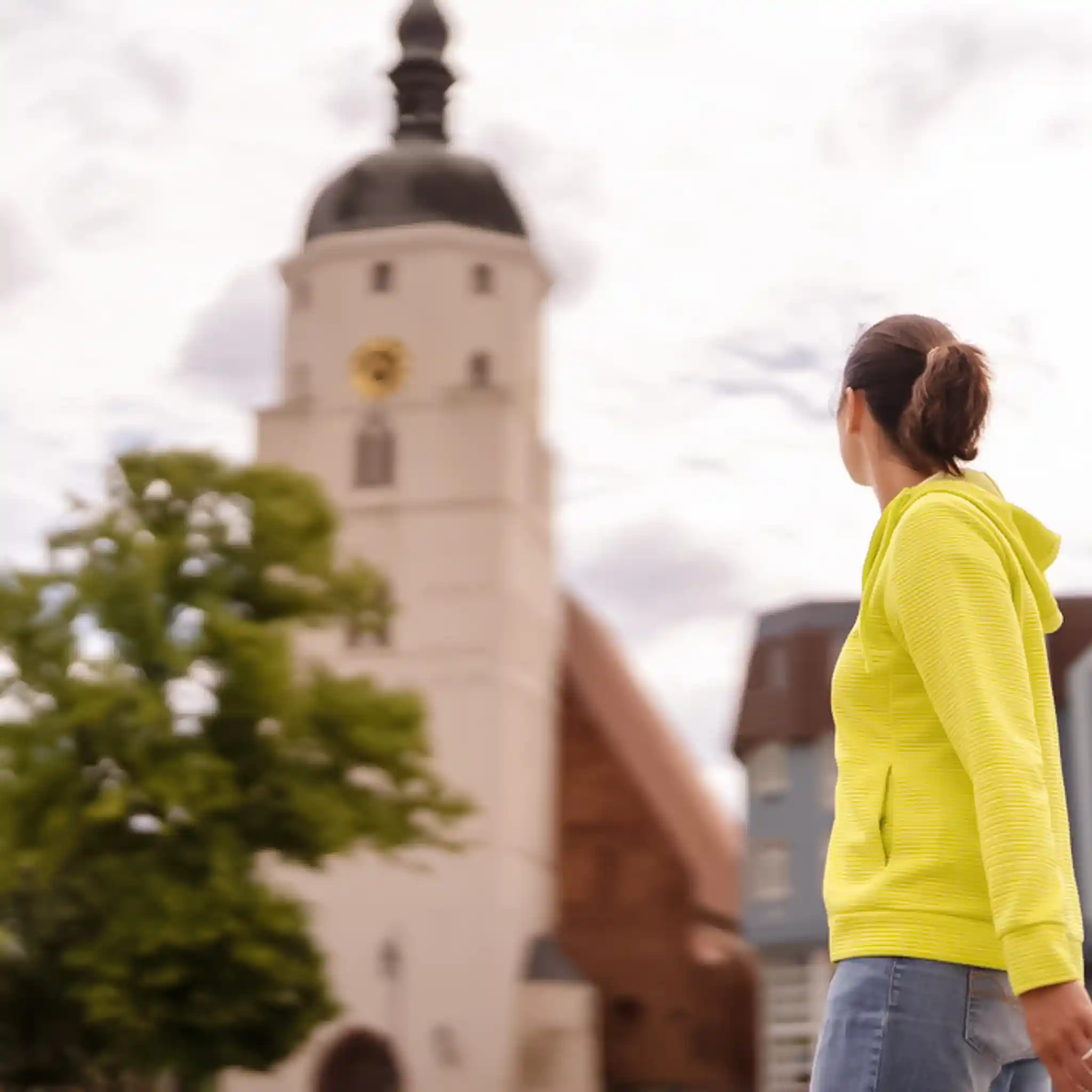 Eine Frau steht seitlich zur Kamera und blickt zu einem Kirchturm.