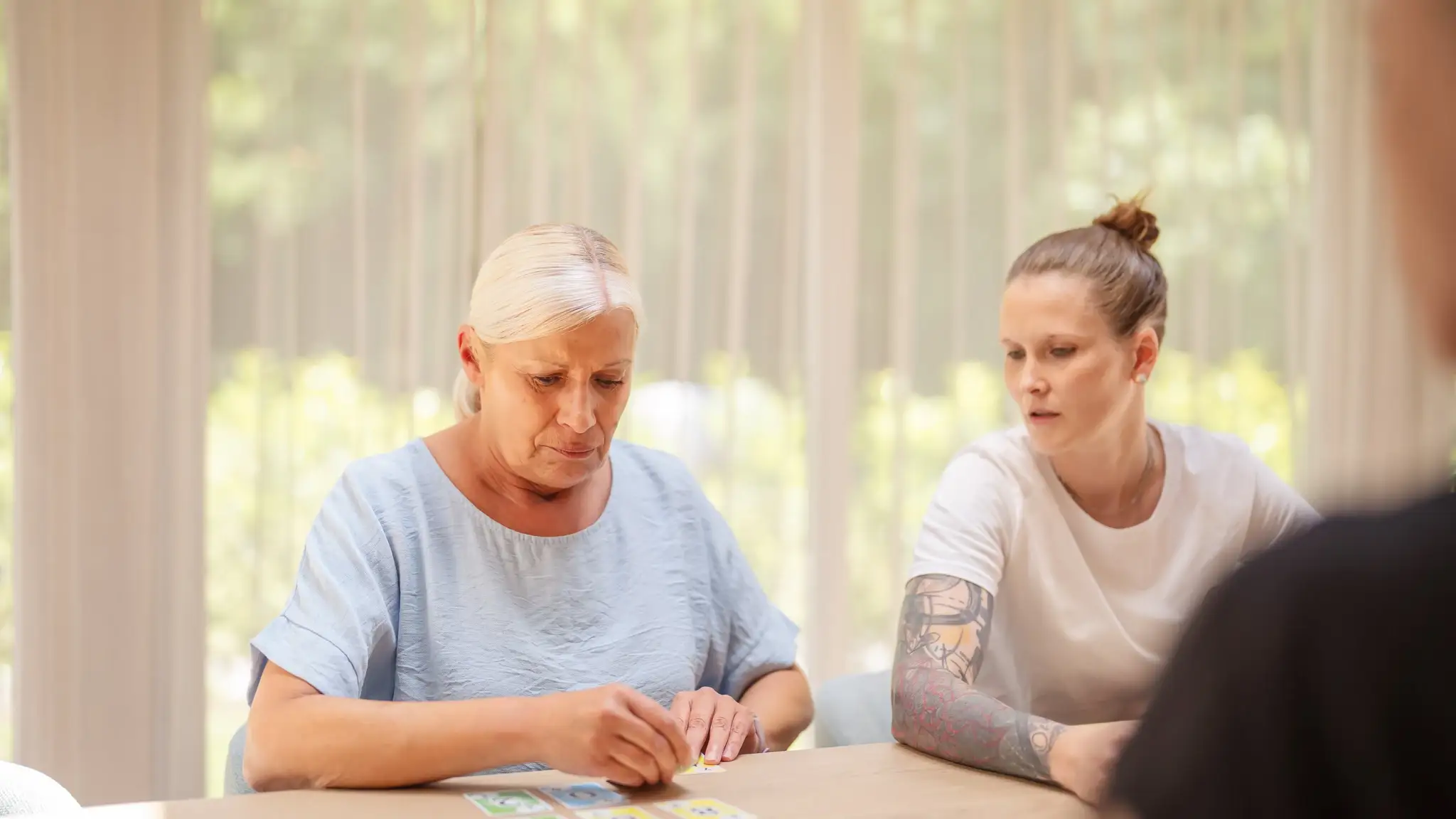 Eine ältere Patientin sitzt mit weiteren Patienten beim Kartenspielen.