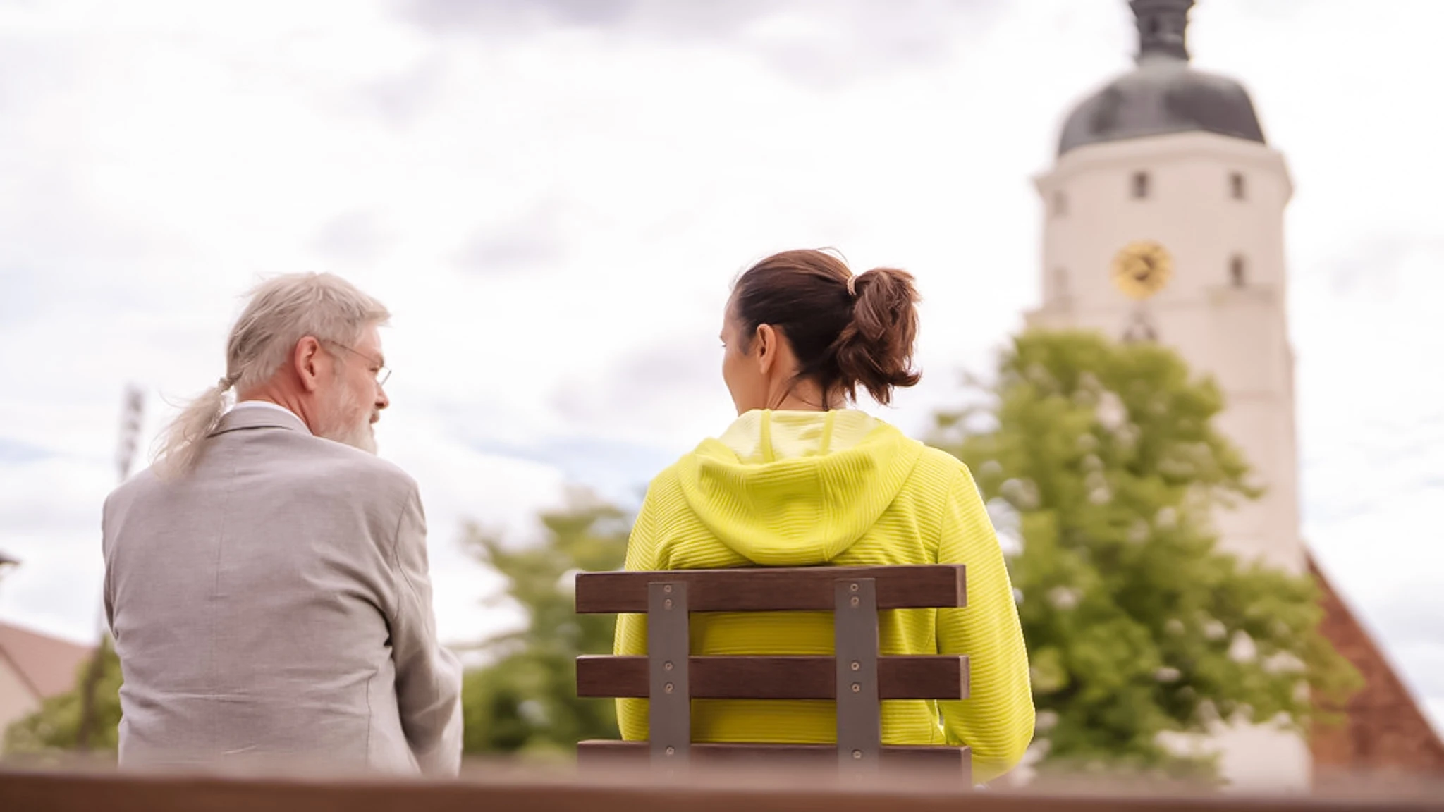Ein Psychiater sitzt neben seiner Patientin auf einer Parkbank. Beide sitzen mit dem Rücken zur Kamera.