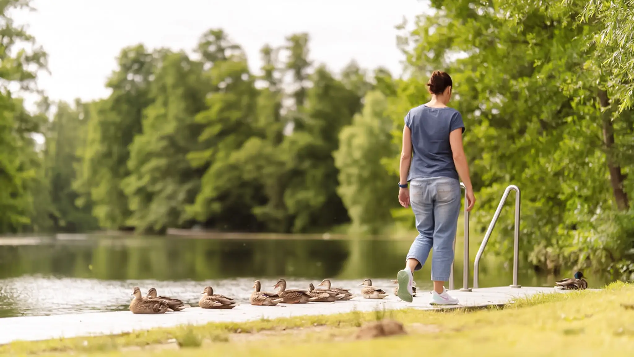 Eine Frau läuft auf einem Steg an Enten vorbei
