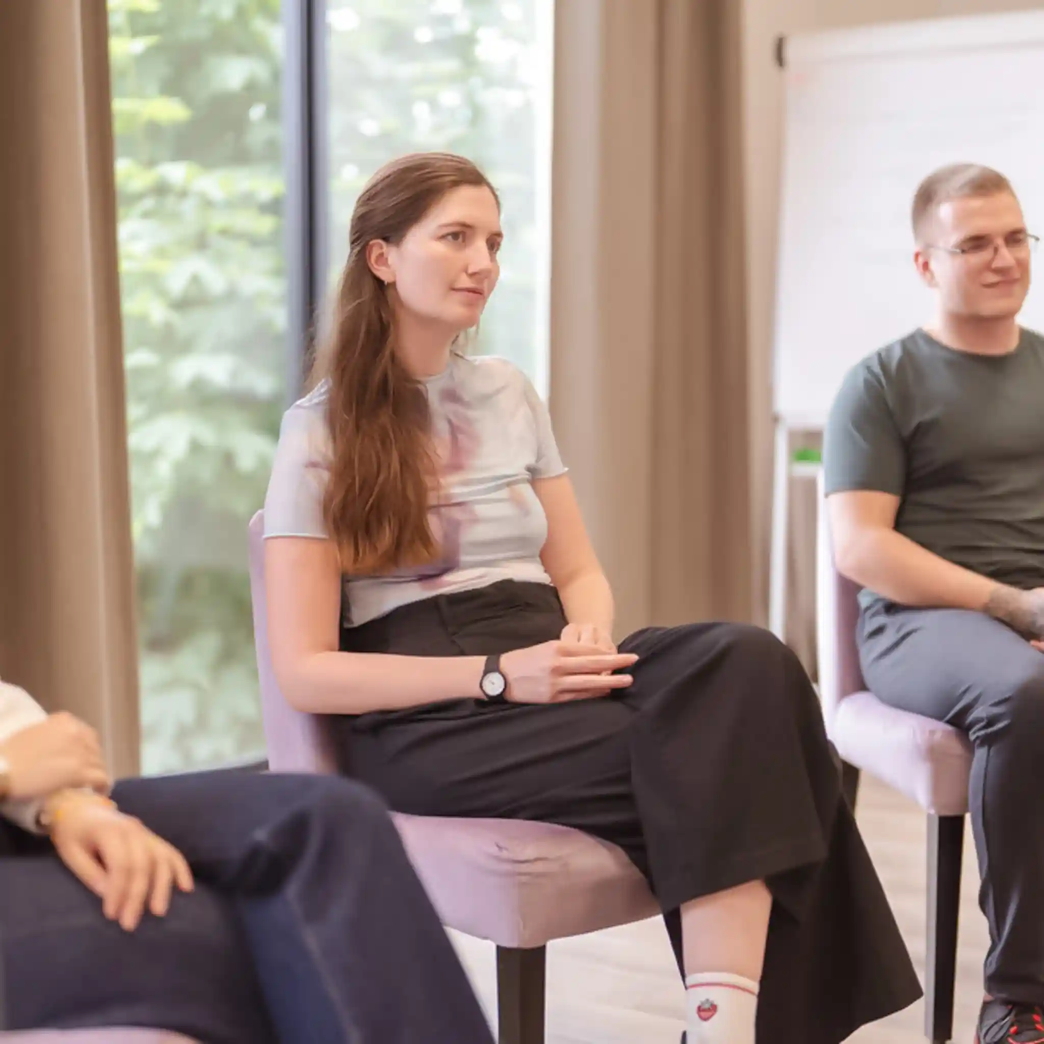 Eine Frau sitzt aufmerksam in einem Stuhl in einem Raum mit Fenster und Vorhängen.