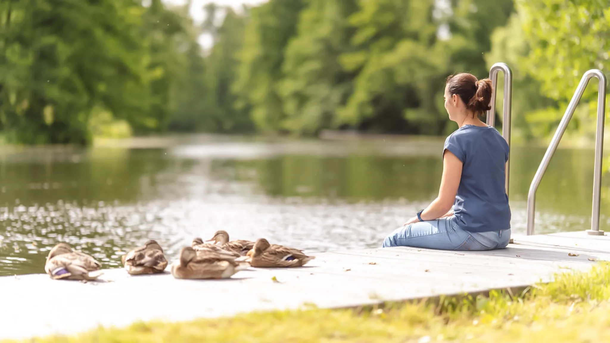 Eine Patientin, die an einer Sommerdepression leidet, sitzt am Ufer eines Flusses neben einigen Enten.