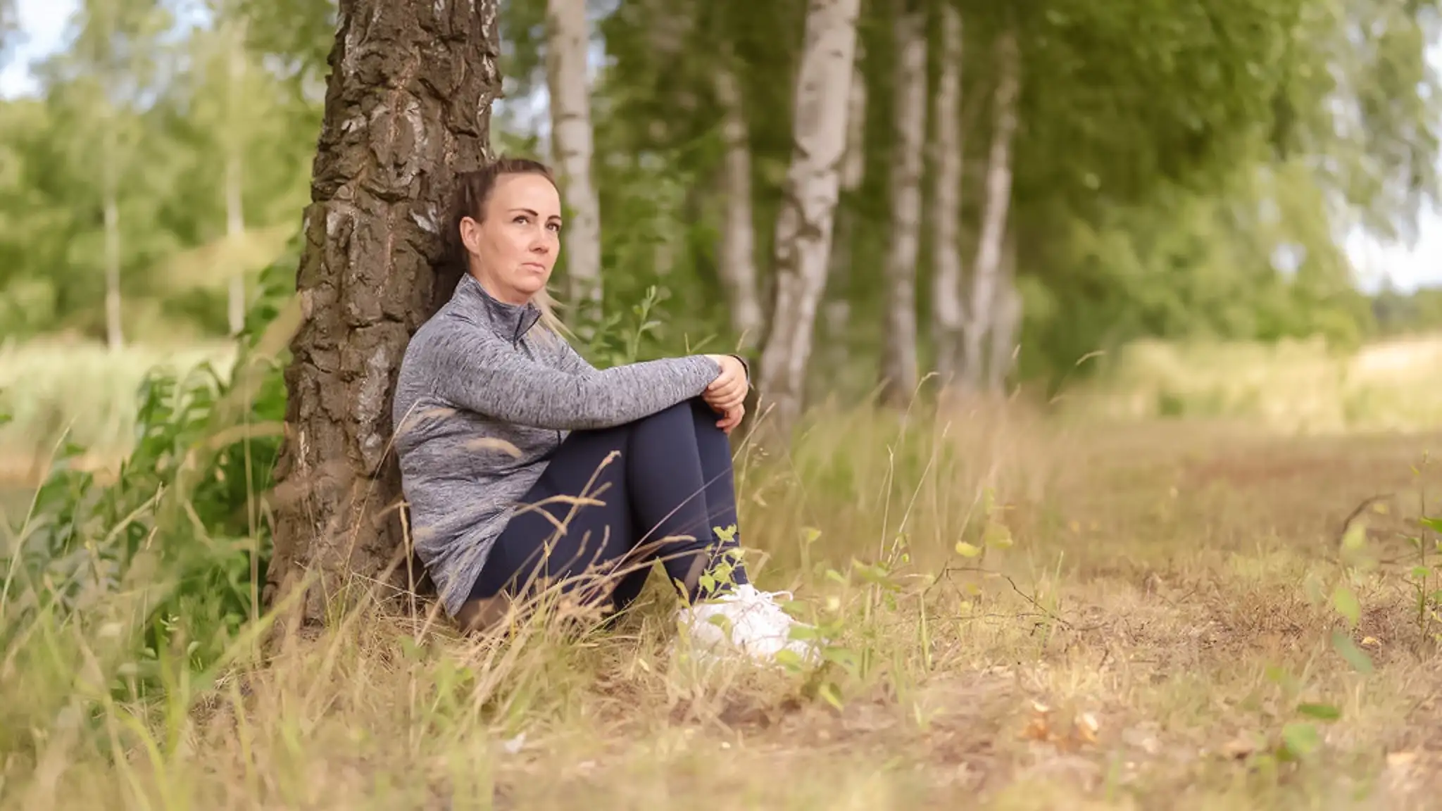 Eine unter ADHS leidende Patientin sitzt auf dem Boden und lehnt an einem Baum.