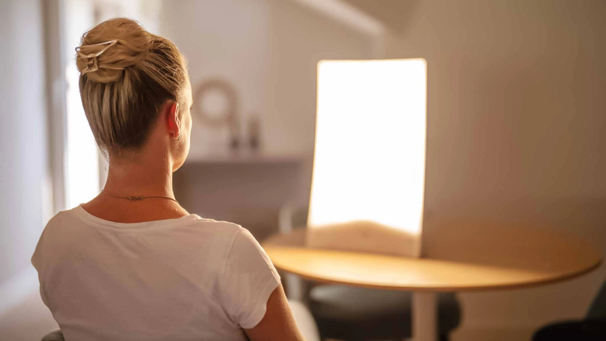 Eine Patientin mit Winterdepression sitzt vor einer Lampe und macht eine Lichttherapie.