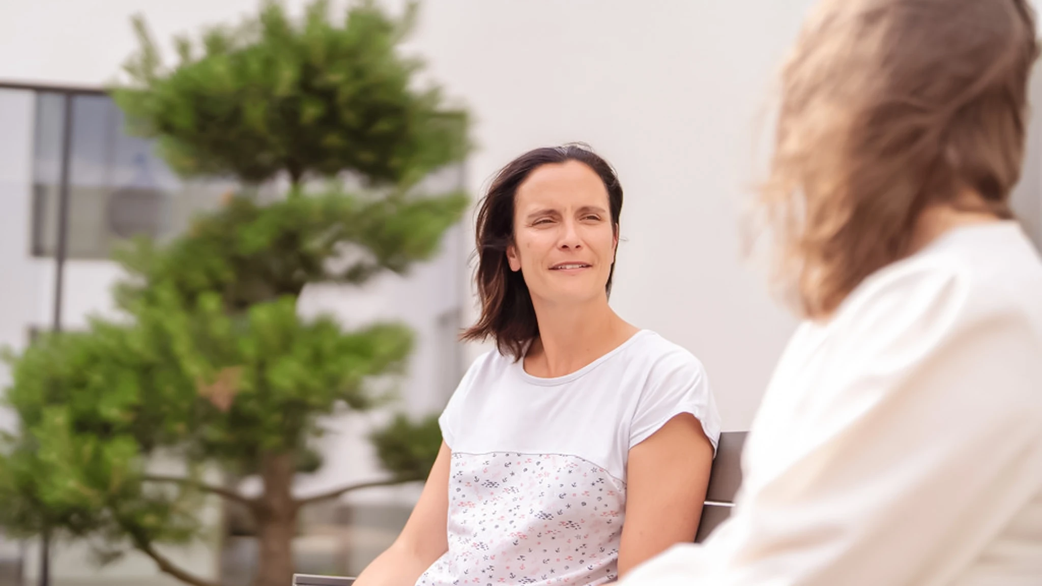 Eine Frau sitzt auf einer Bank im Innenhof einer Vincera Klinik neben einer anderen Patientin.