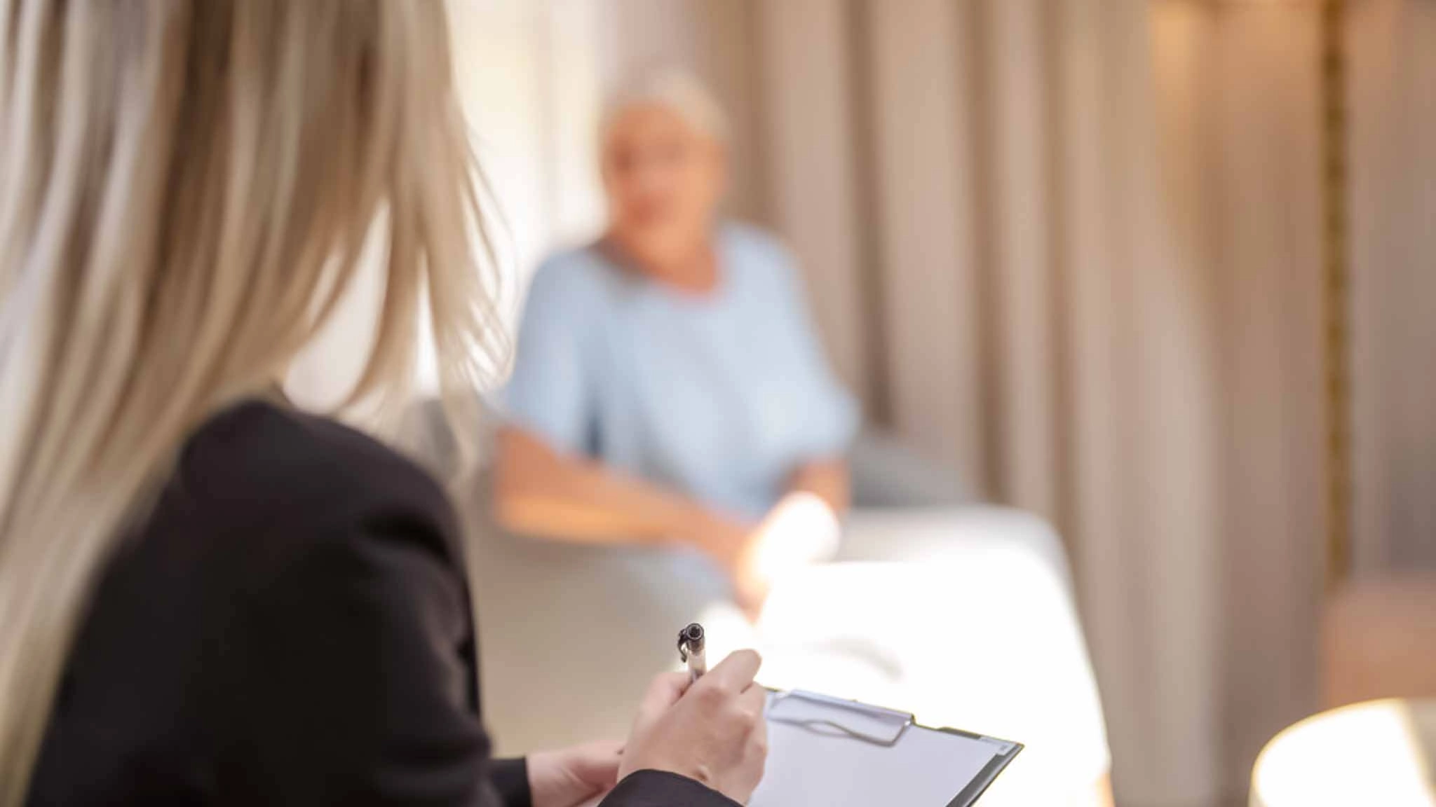 Eine Psychotherapeutin sitzt mit einem Klemmbrett in einer Therapiesitzung mit einer Patientin.