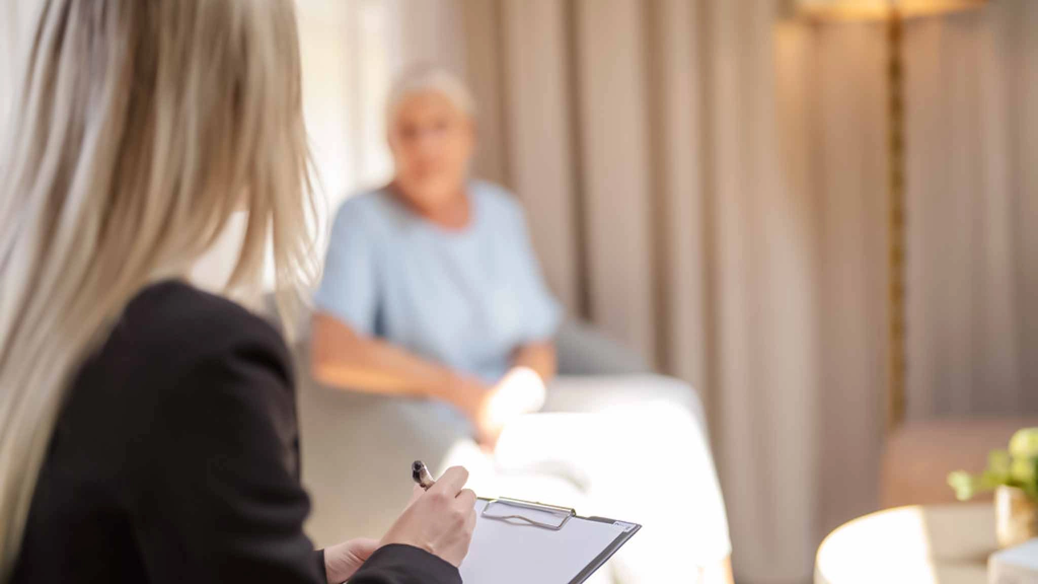 Eine Psychotherapeutin hält ein Klemmbrett für Notizen während einer Therapiesitzung mit einer Patientin, die mit den Folgen der Wechseljahre kämpft.