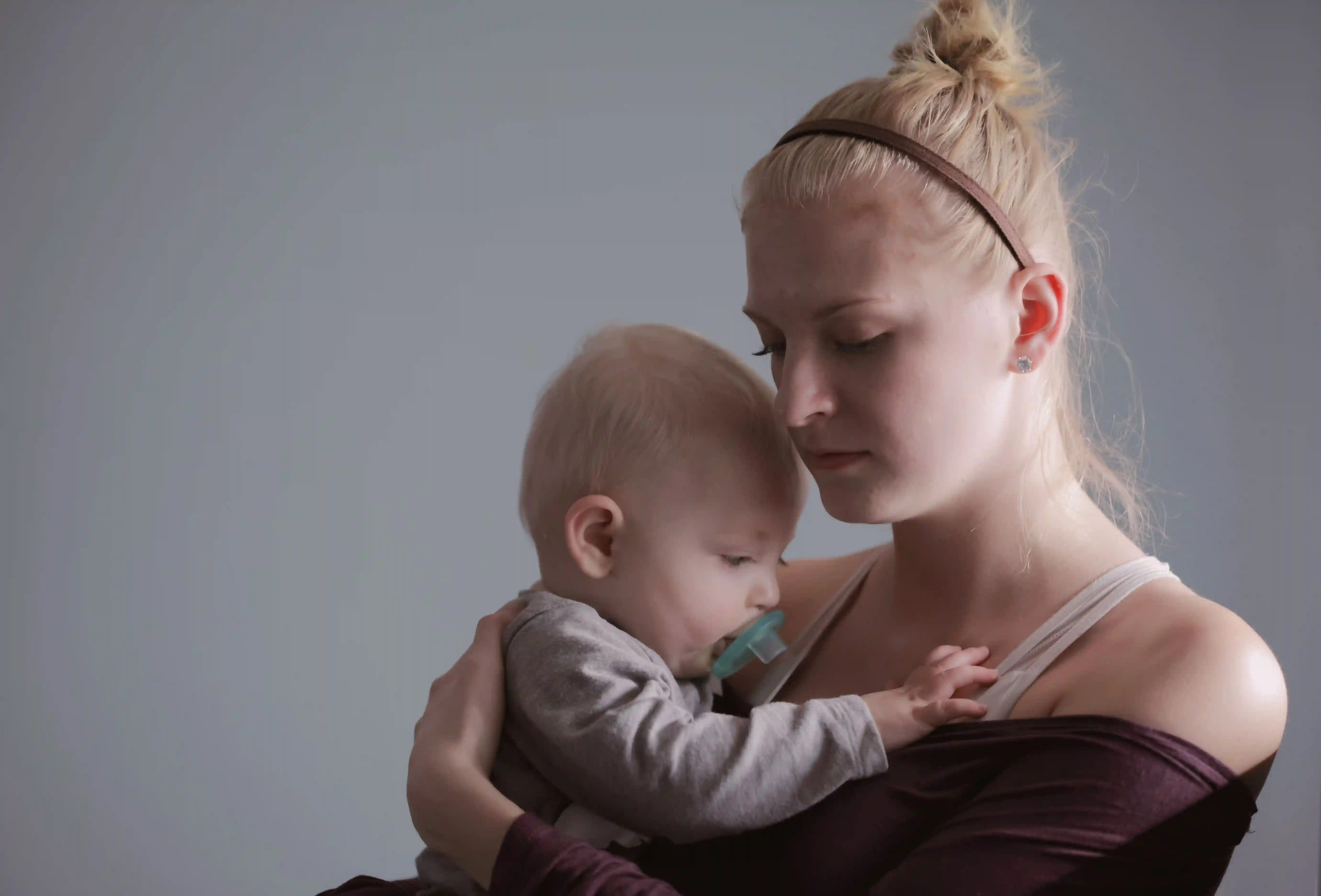 Eine junge Frau mit postpartaler Depression hält ihr Baby im Arm.