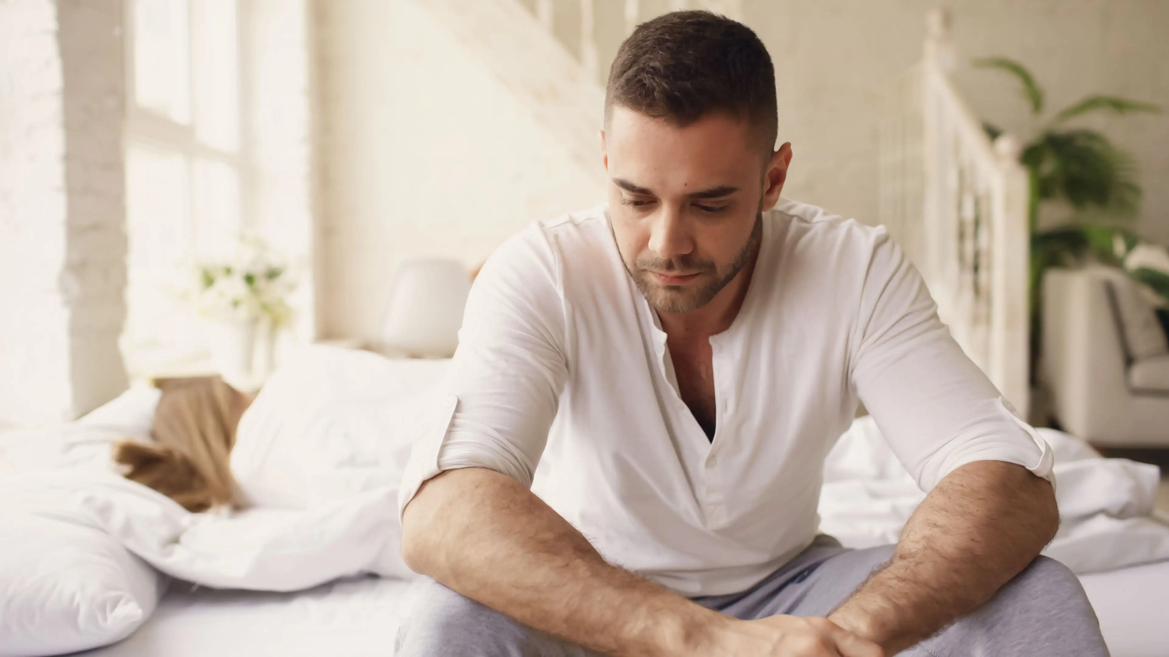 Mann mit Depressionen nach der Geburt seines Kindes sitzt auf dem Bett und schaut nachdenklich nach unten.