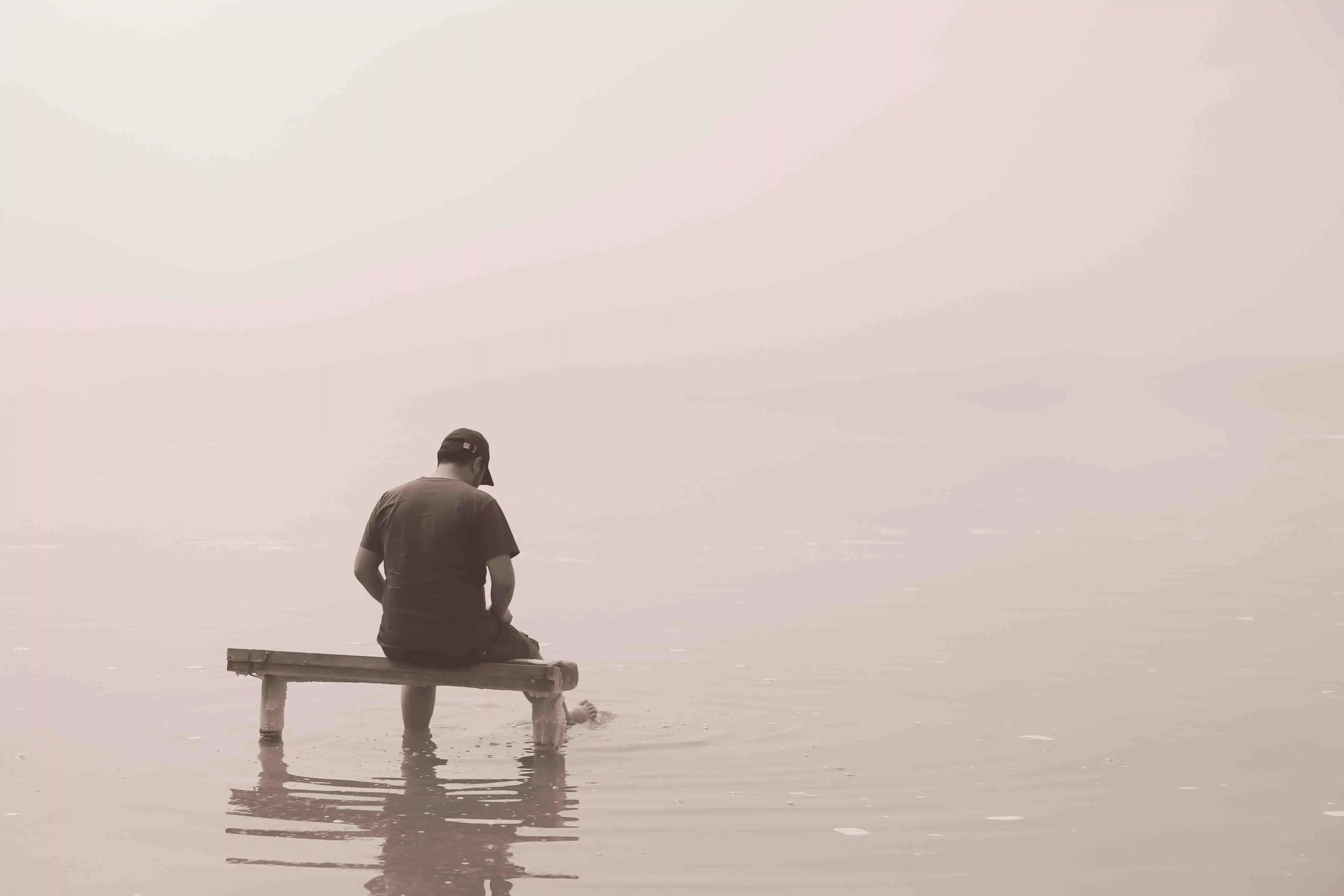 Ein depressiver Patient sitzt auf einer Bank im Wasser.
