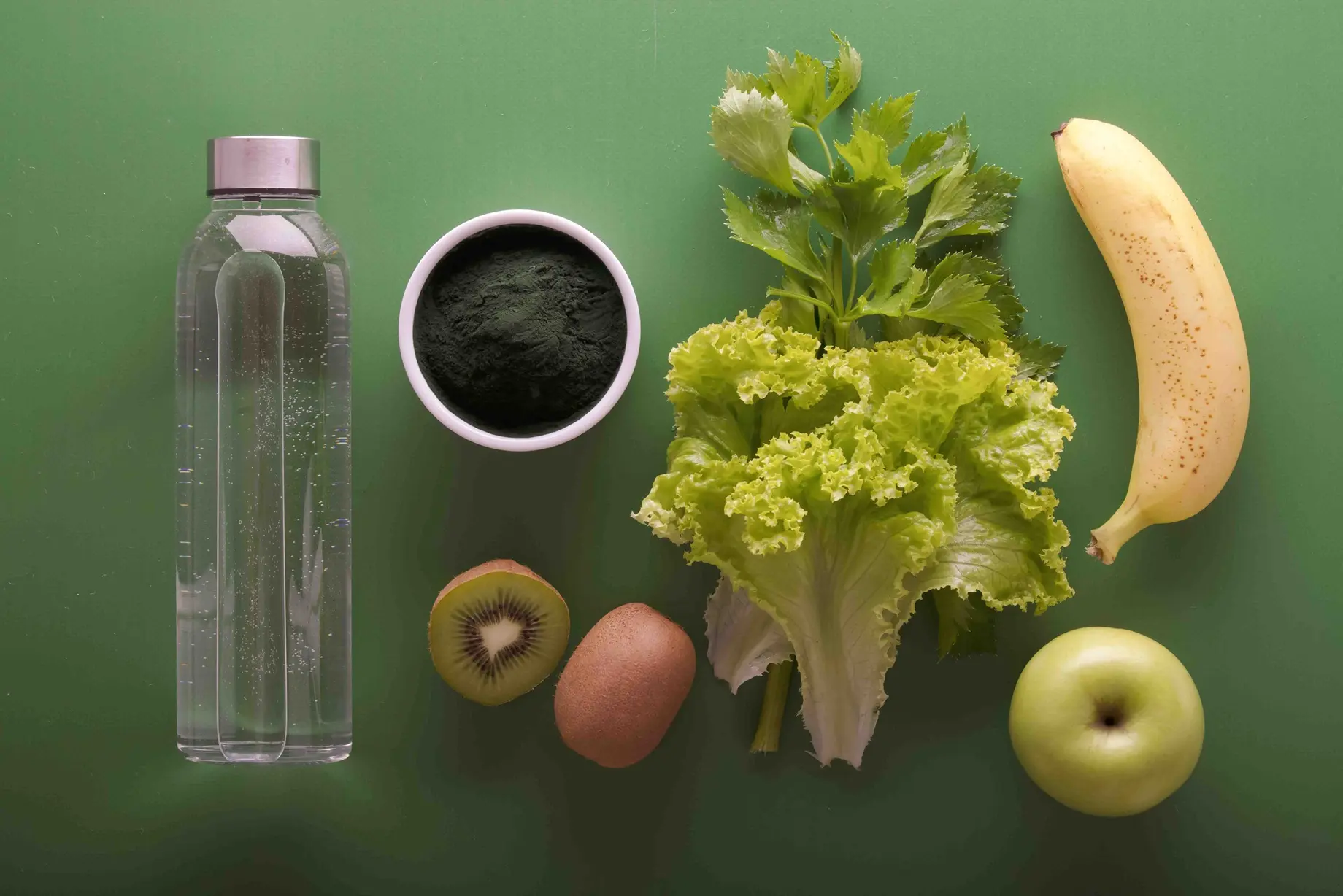 Eine Flasche Wasser liegt zusammen mit einem Salatblatt und einigen Früchten auf einem grünen Untergrund.