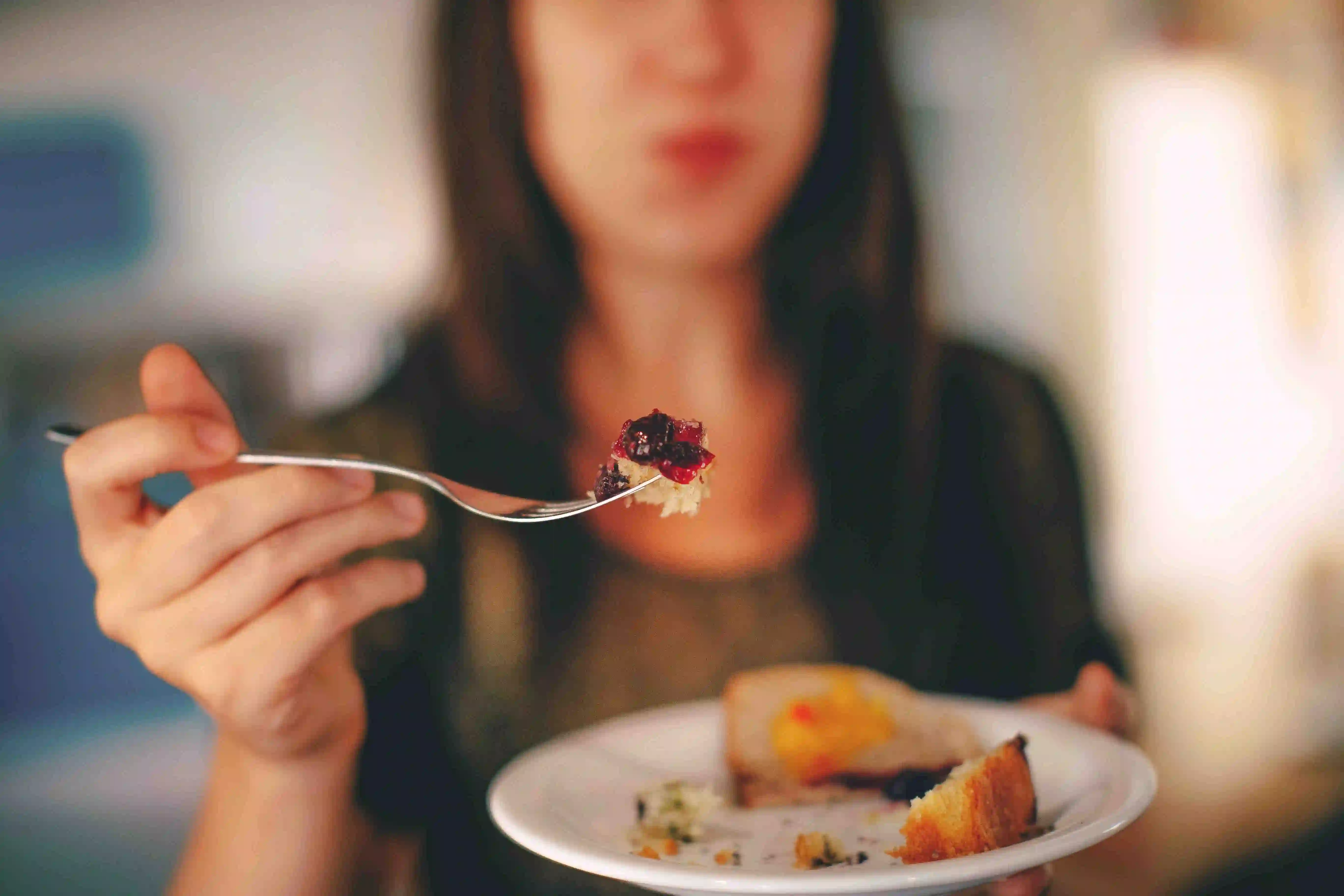 Eine Frau hält einen Teller mit Essen und eine Gabel mit einem Stückchen Kuchen.