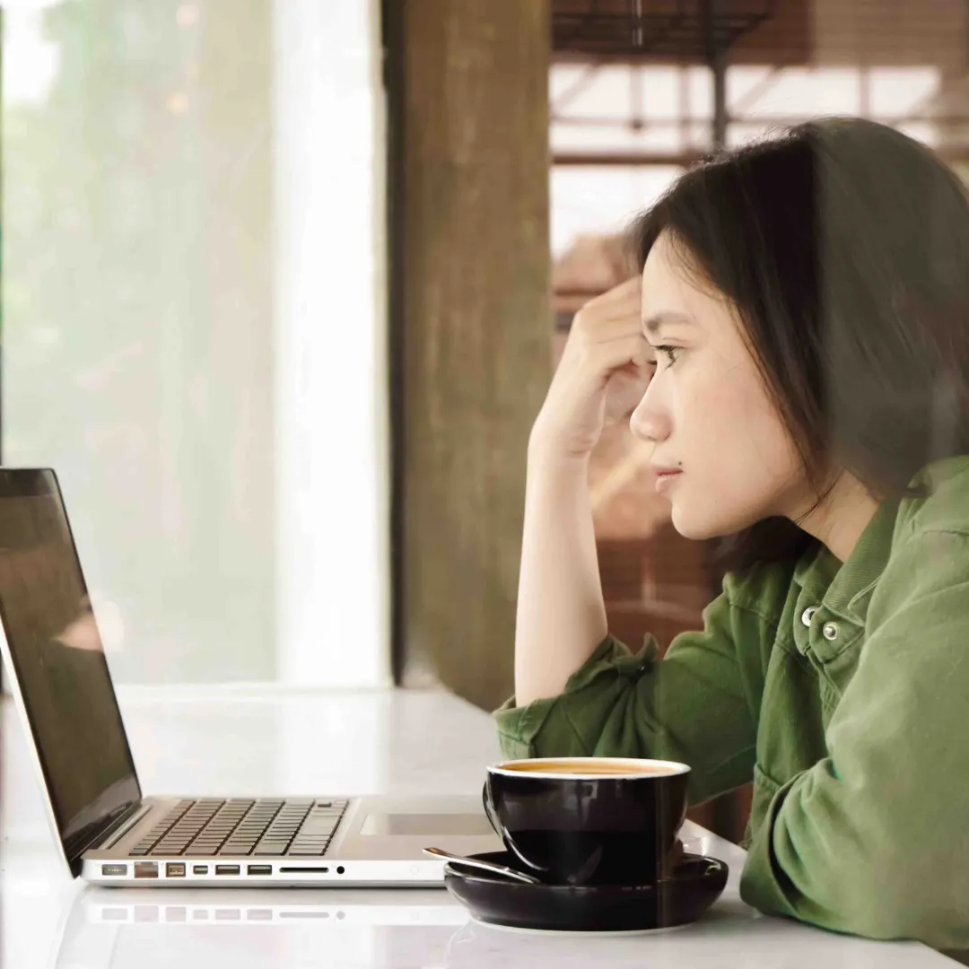 Eine junge Frau in Führungsposition mit Depressionen sitzt vor ihrem Laptop.