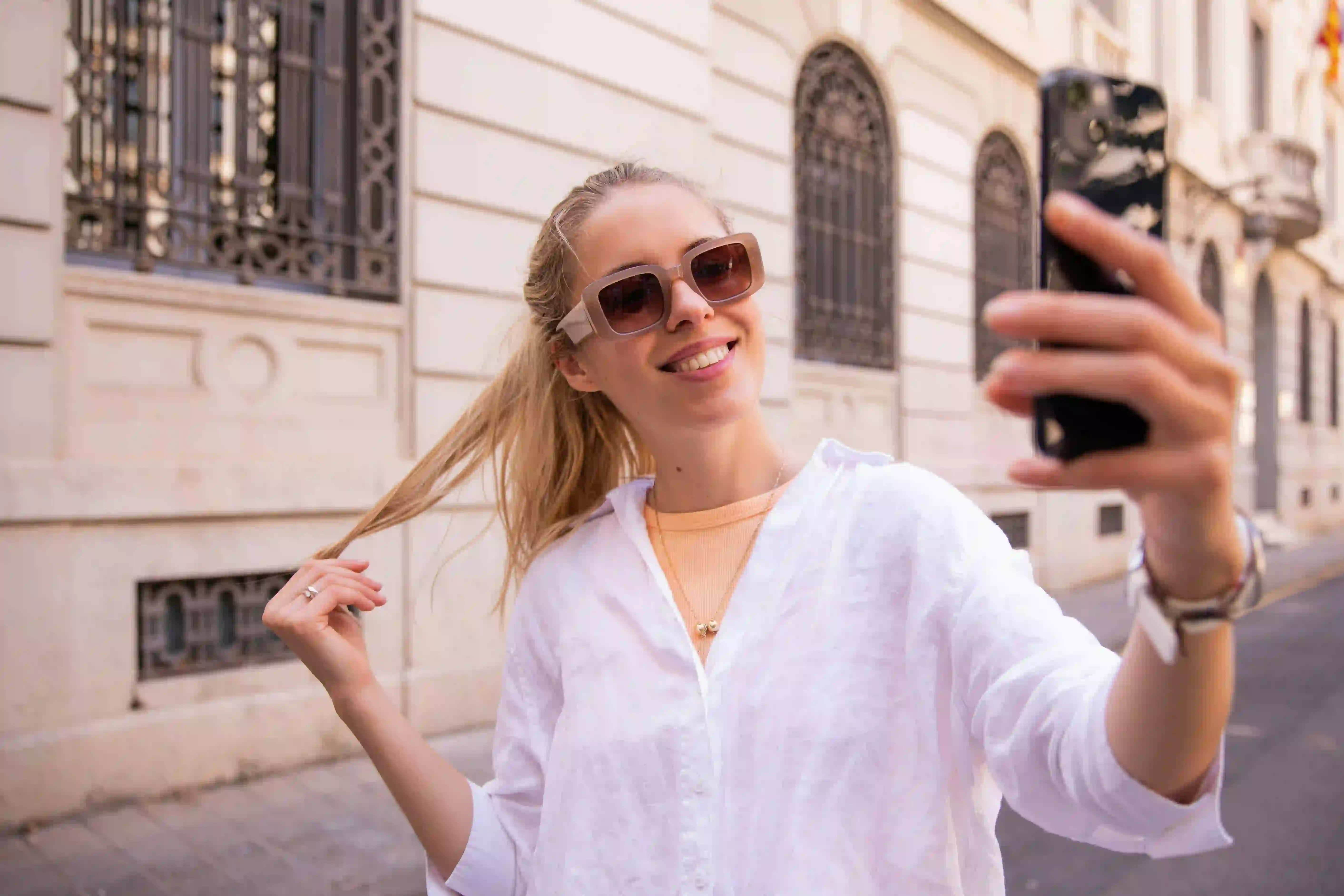 Eine blonde Frau in weißem T-Shirt macht ein Selfie