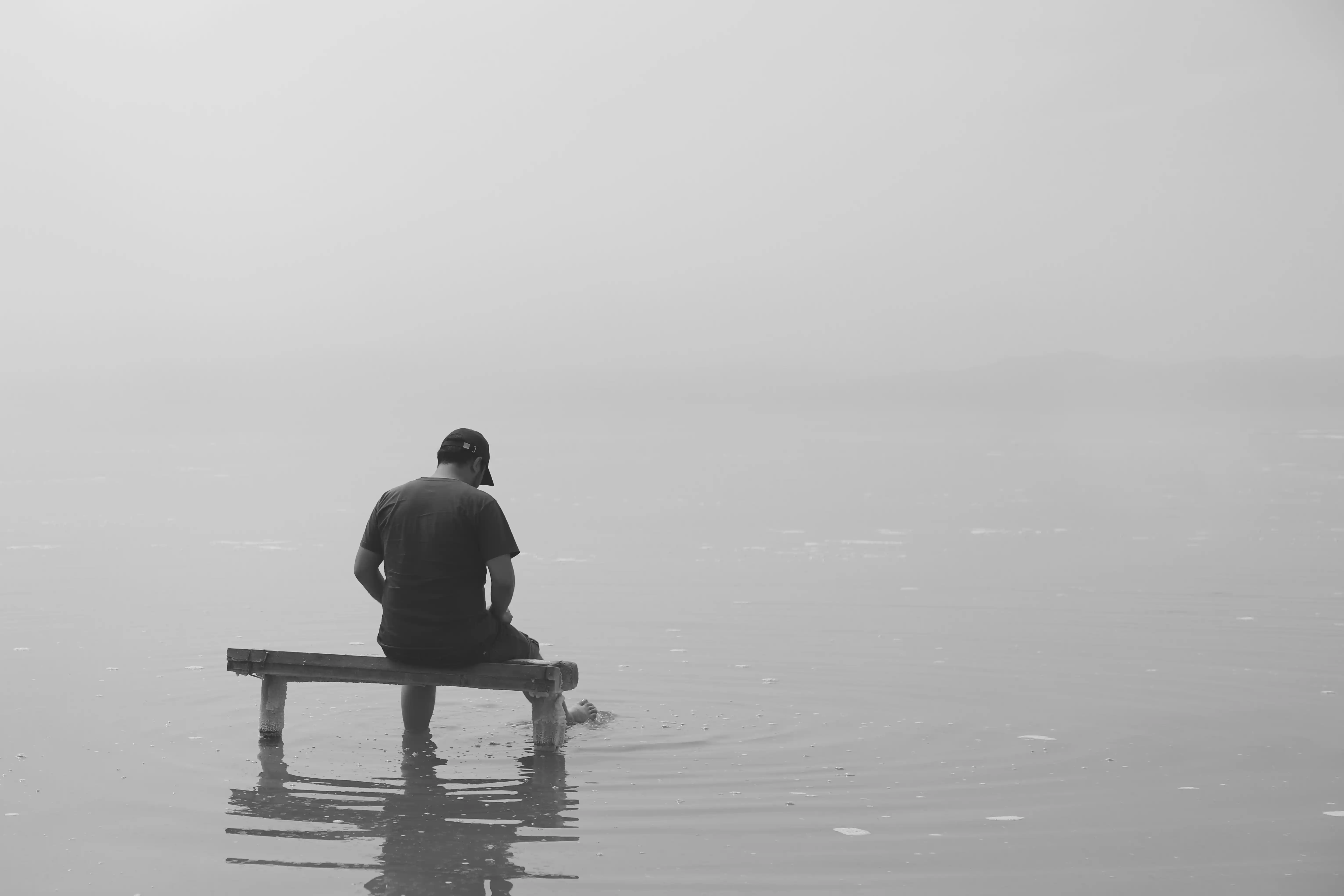Ein Mann sitzt auf einer Bank im flachen Wasser eines Sees