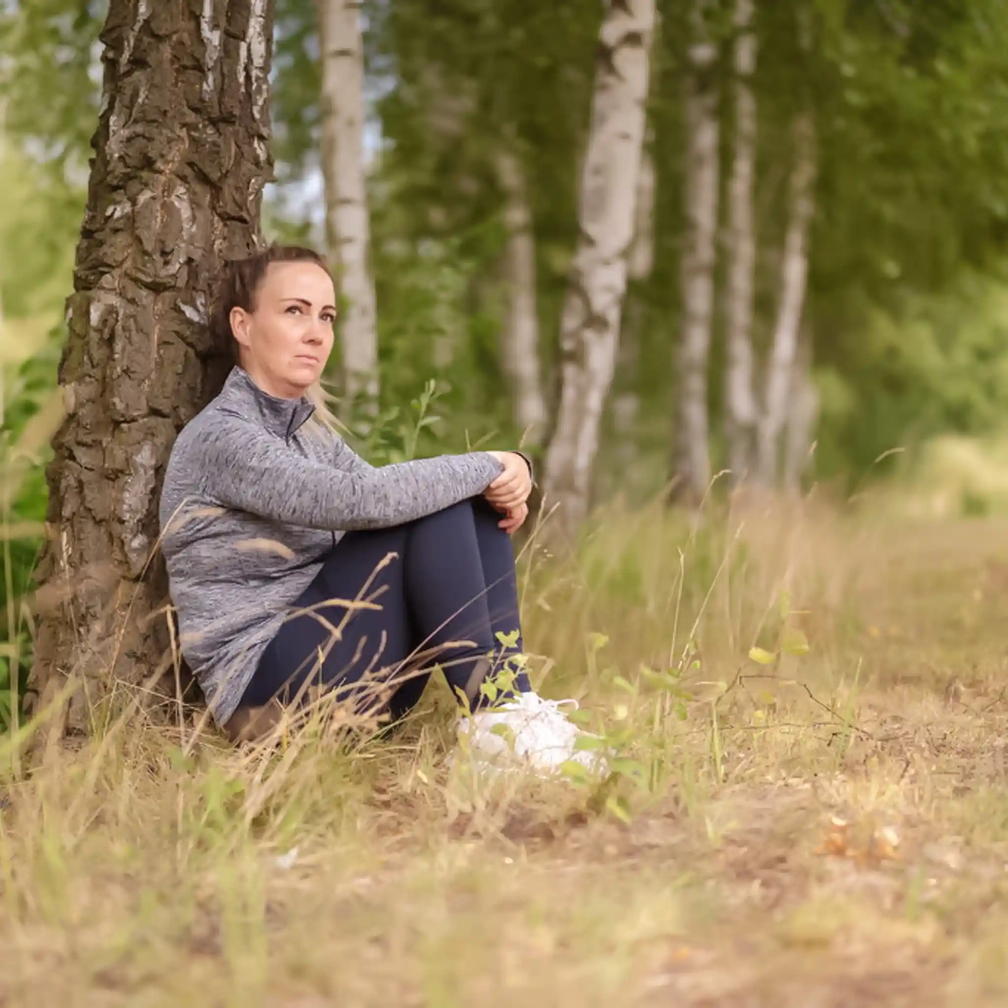 Eine Frau lehnt sitzend an einem Baum und schaut in die Ferne