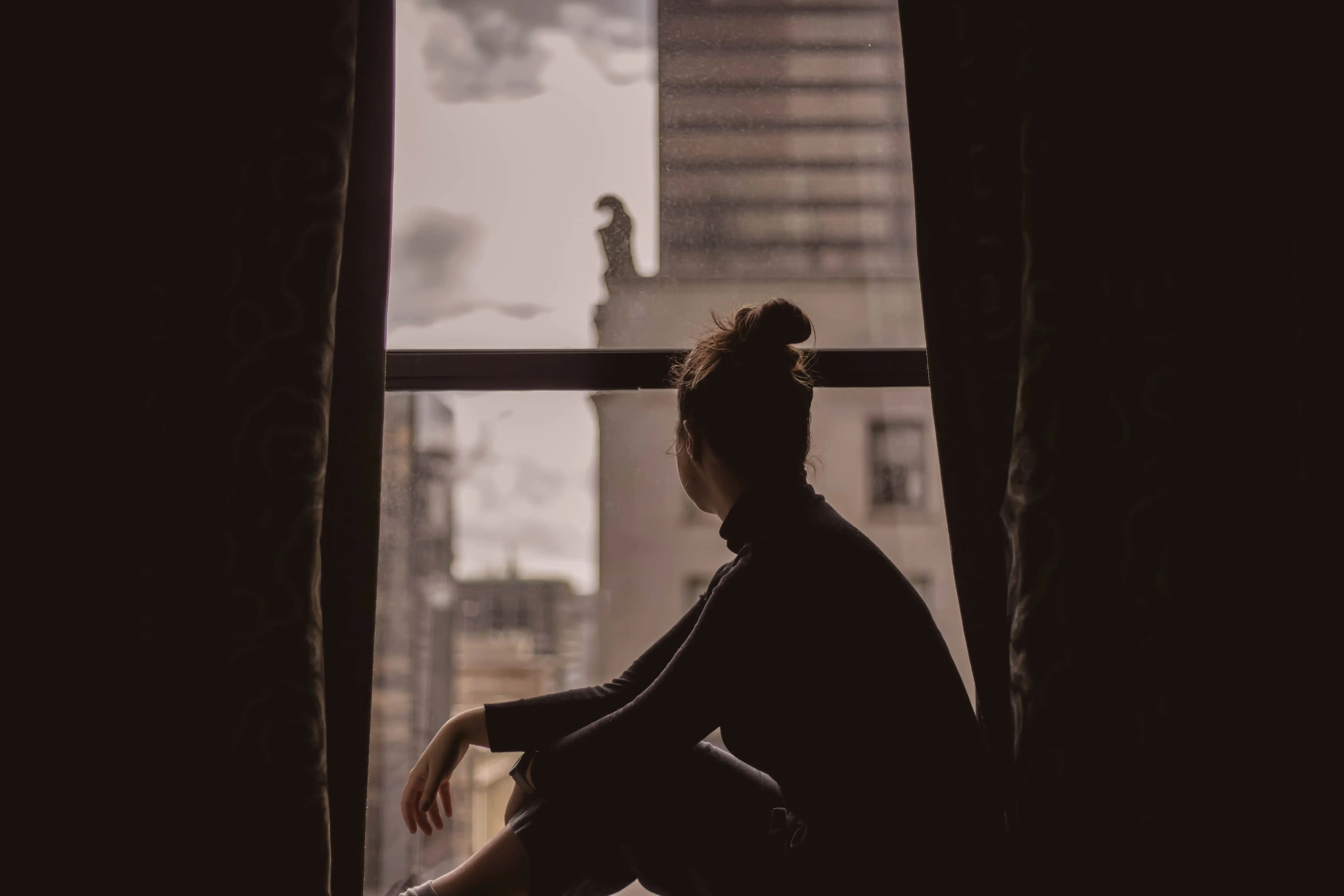 Eine Frau sitzt auf der Fensterbank und schaut aus dem Fenster