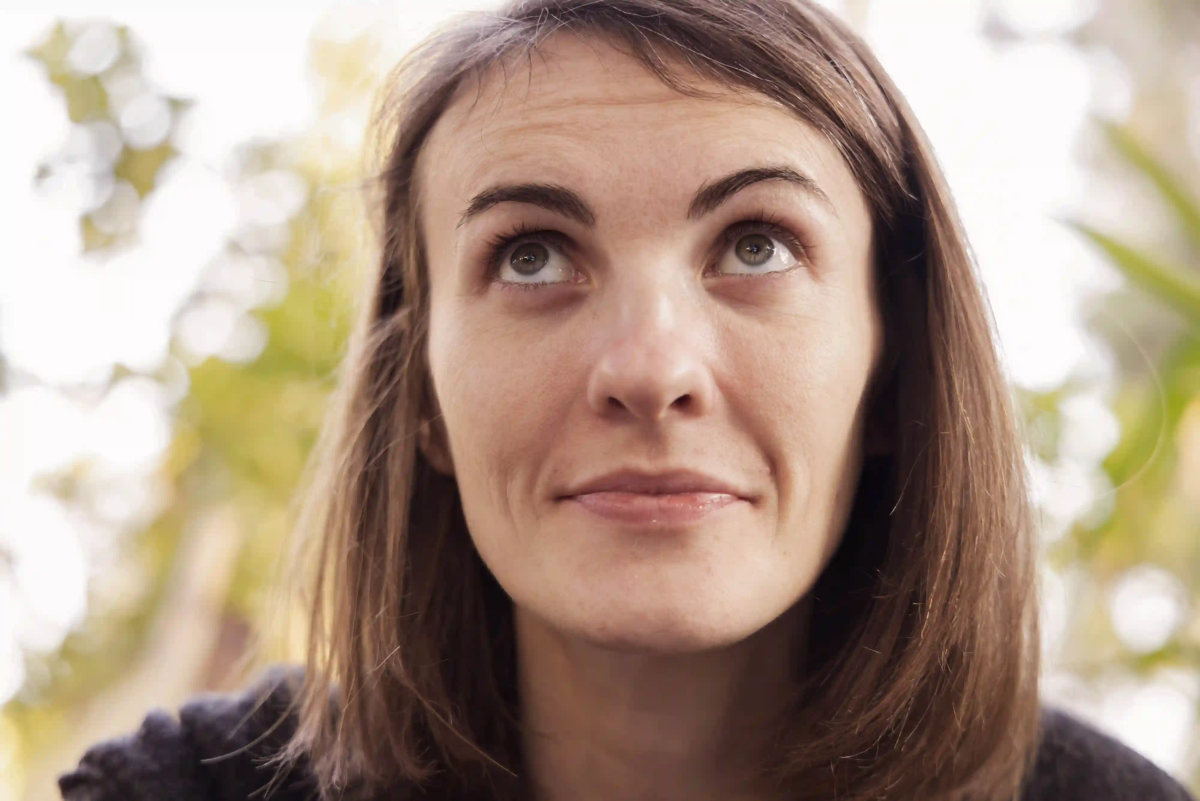Nahaufnahme des Gesichts einer brünetten Frau, die mit einem leichten Lächeln nach oben blickt.