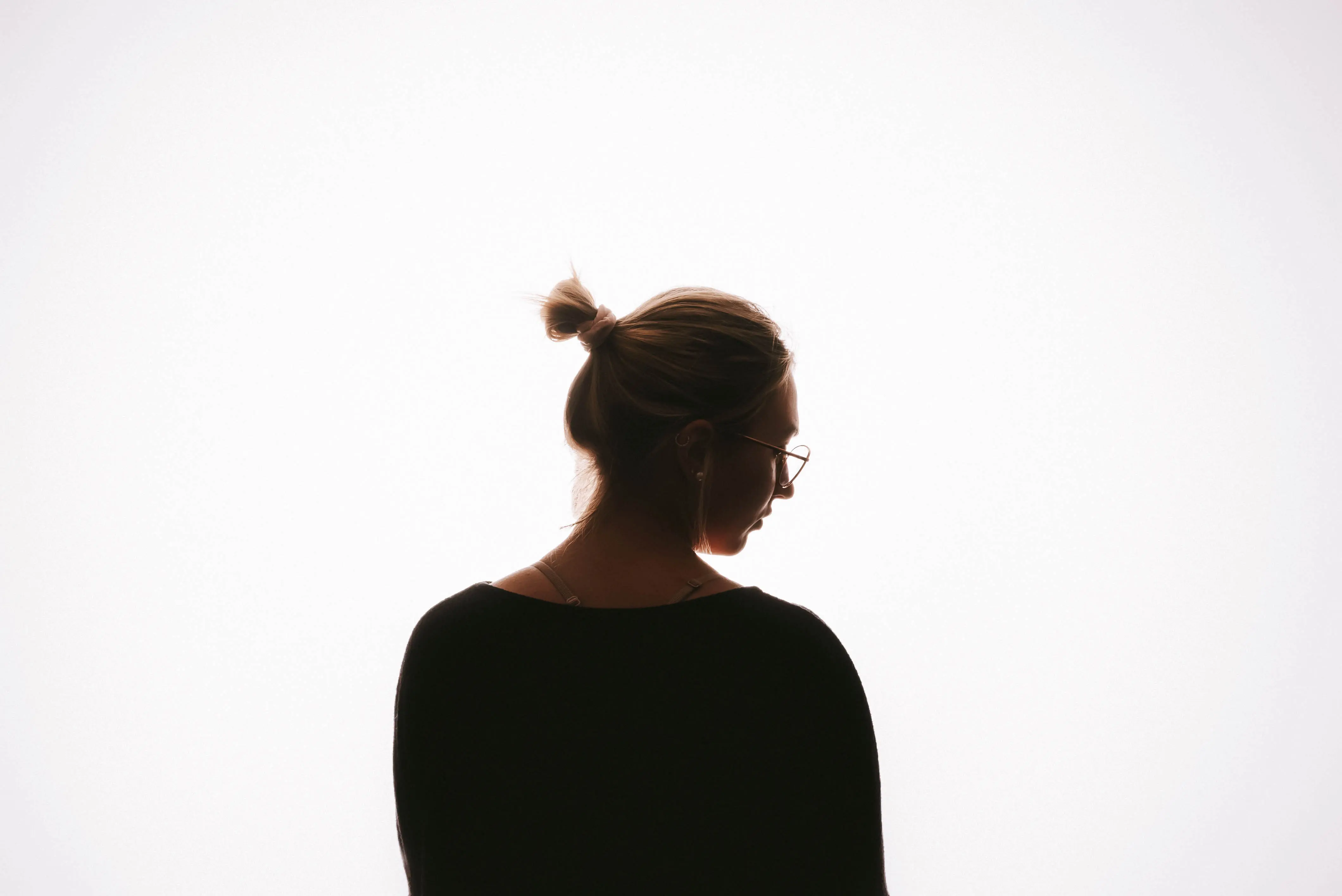 Silhouette einer Frau mit Brille und Dutt im dunklen Oberteil vor einem strahlend weißen Hintergrund.