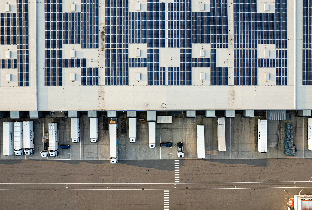 Nachhaltige Immobilie mit Photovoltaikanlage auf dem Dach und mehreren LKWs im Ladebereich.