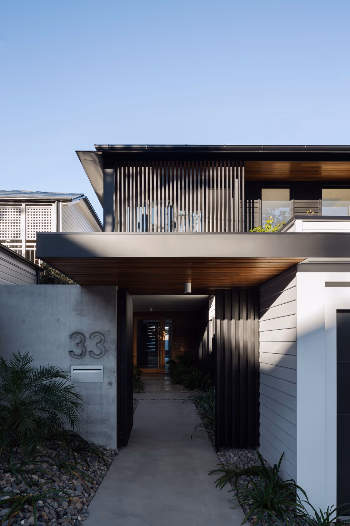 Modern house facade with black slats, white siding, a concrete wall, and a landscaped path.