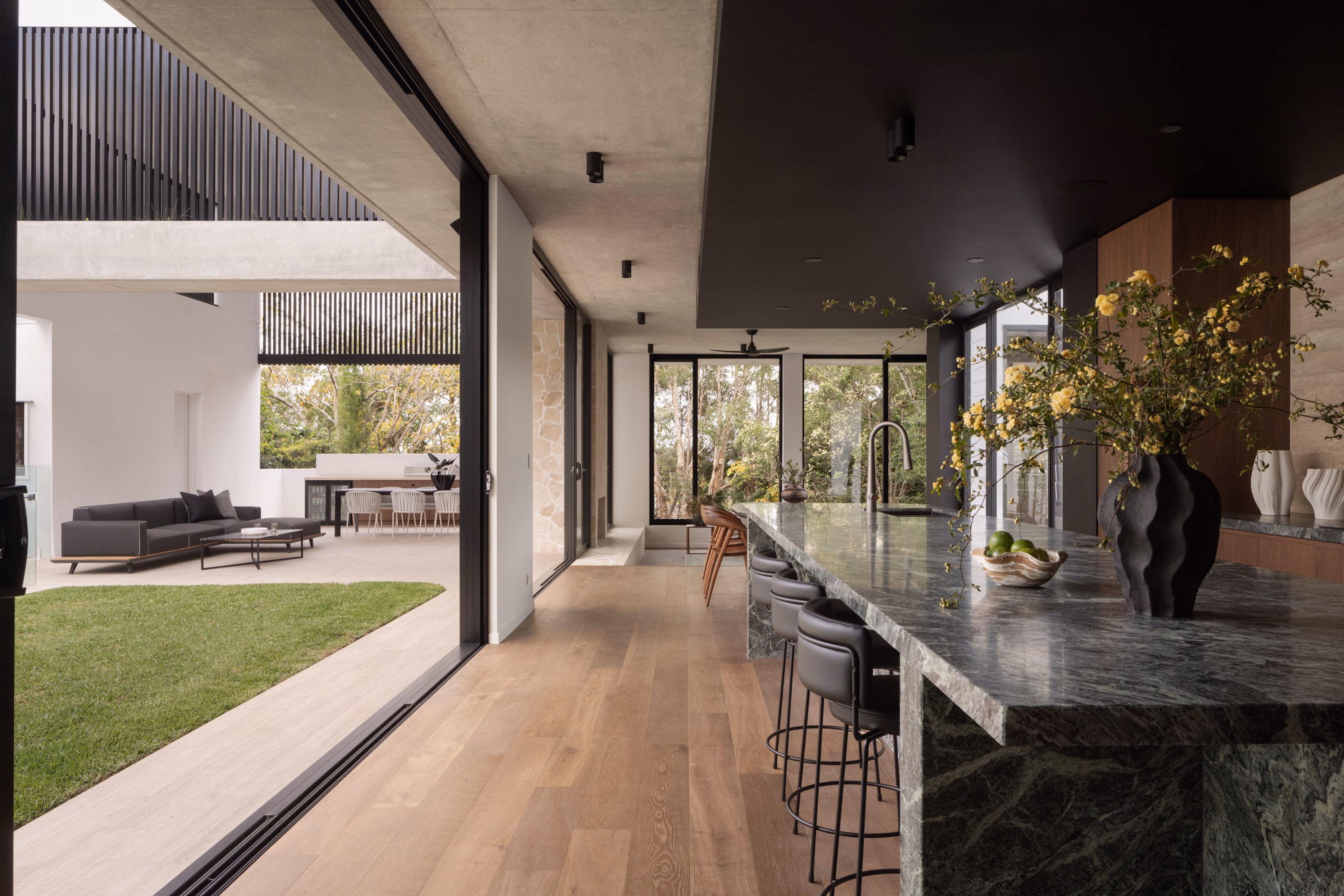 Open-plan kitchen at Stanley with a green marble island, walnut cabinetry, black ceiling, and seamless connection to the outdoor entertaining area.