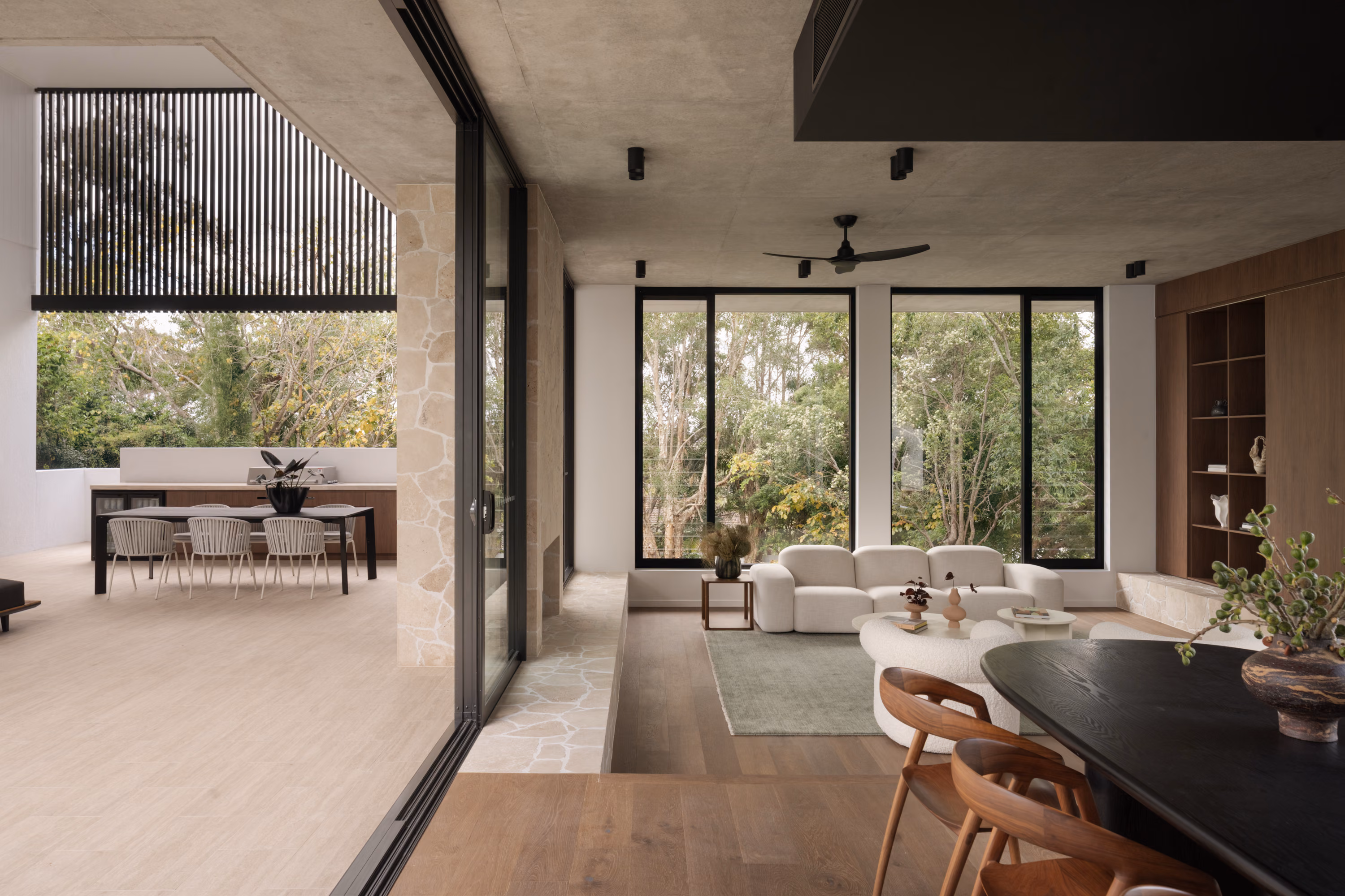 Open living and dining area at Stanley with floor-to-ceiling glazing, custom walnut shelving, and views to the outdoor entertaining terrace.