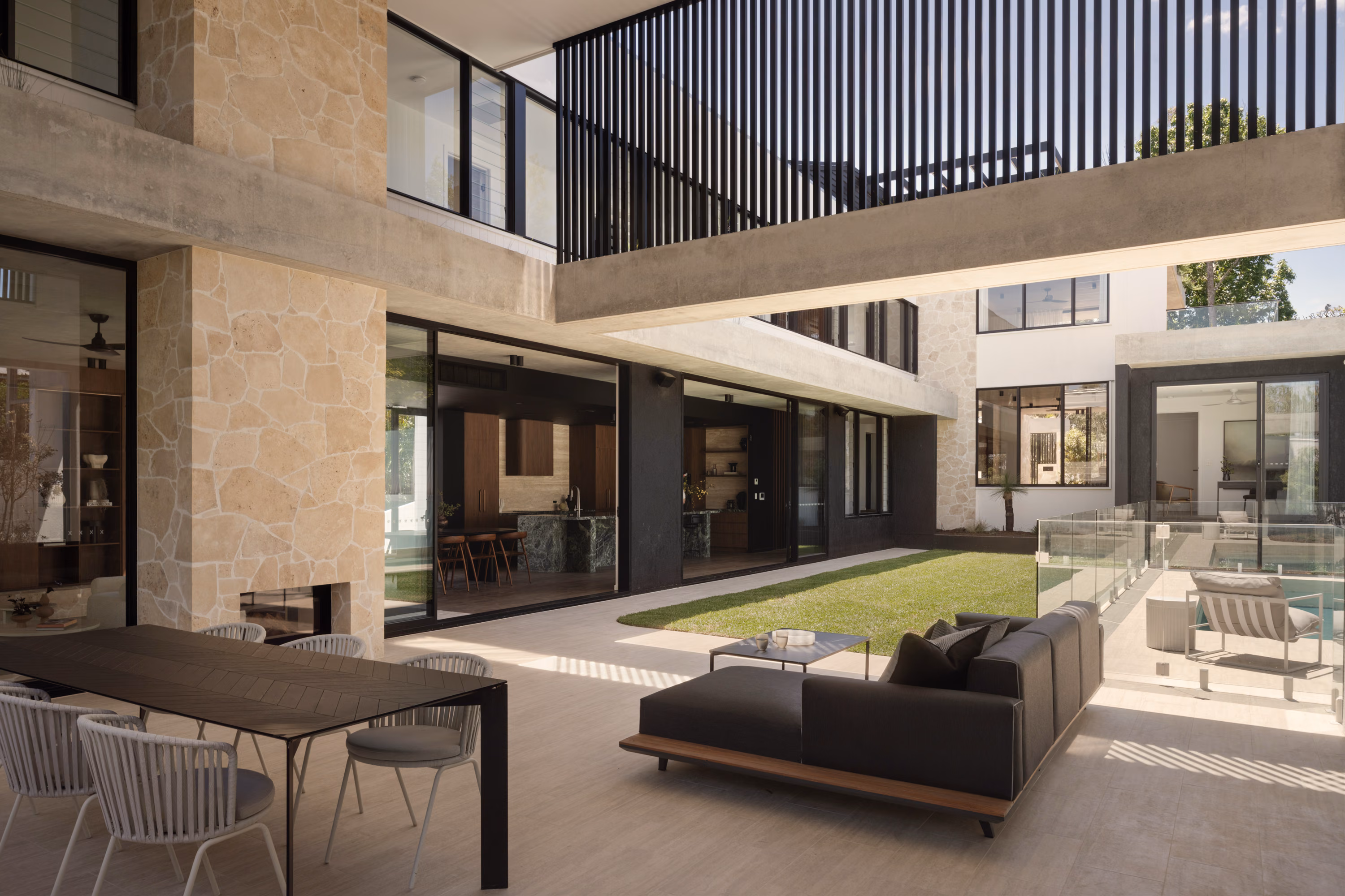 Covered outdoor entertaining terrace at Stanley with dining table, lounge seating, outdoor kitchen, and views across the central courtyard.