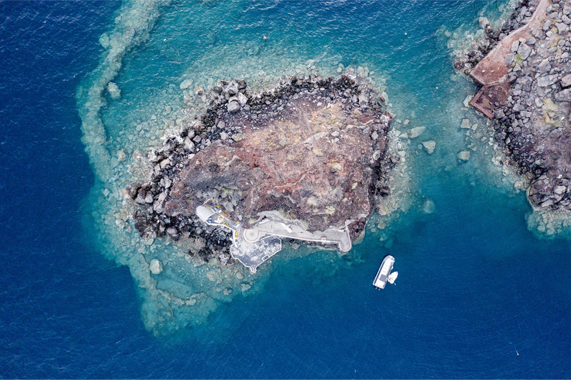 Felsige Insel vor Santorini im türkisblauen Meer aus der Luft