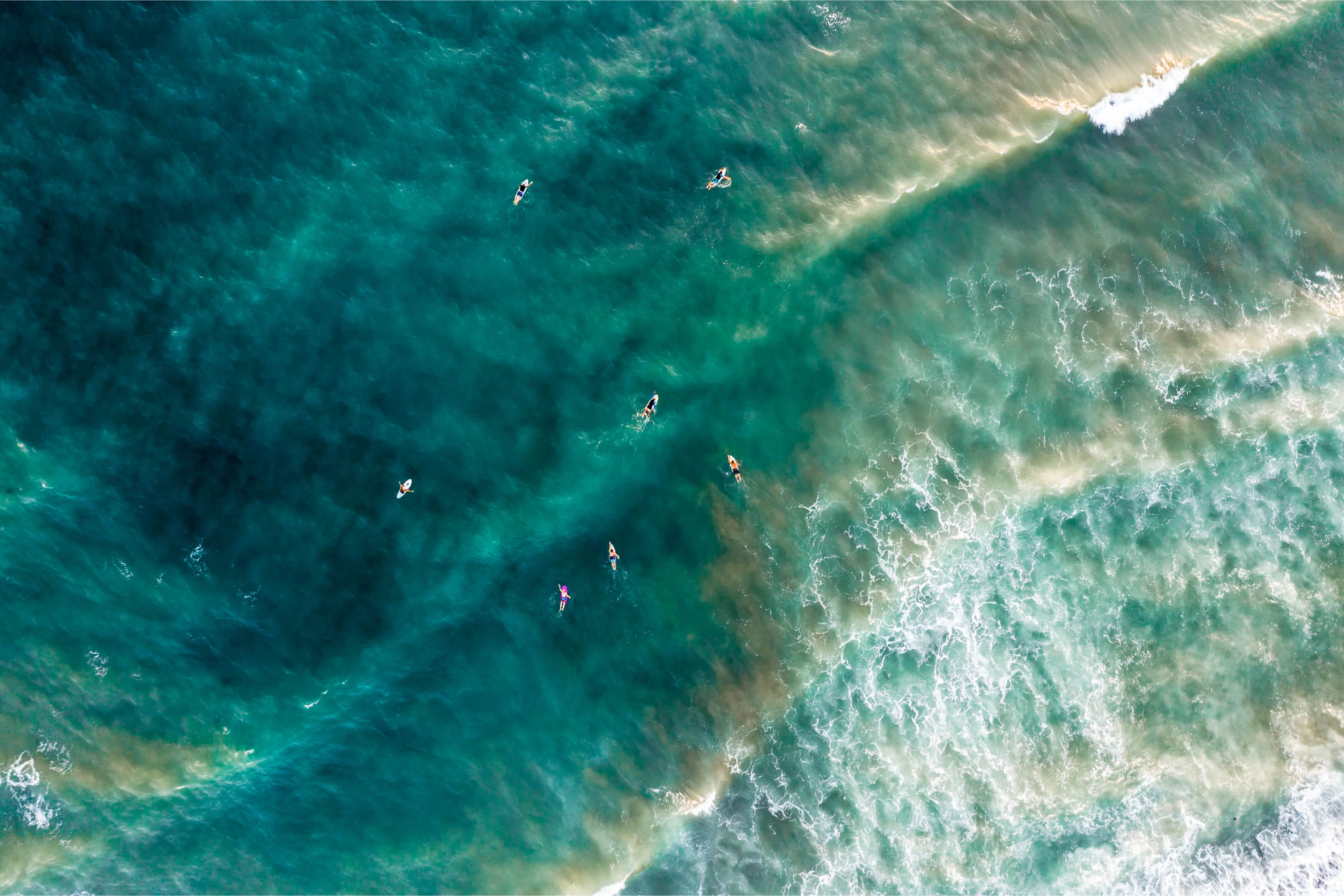 Surfer zwischen brechenden Wellen vor der Küste aus der Luft