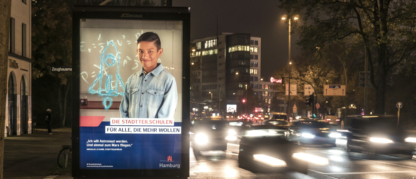 Citylight der Kampagne für die Hamburger Stadtteilschulen mit Astronautenmotiv bei Nacht