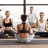 Vier Personen sitzen auf Yogamatten in einem hellen Raum und meditieren im Schneidersitz.