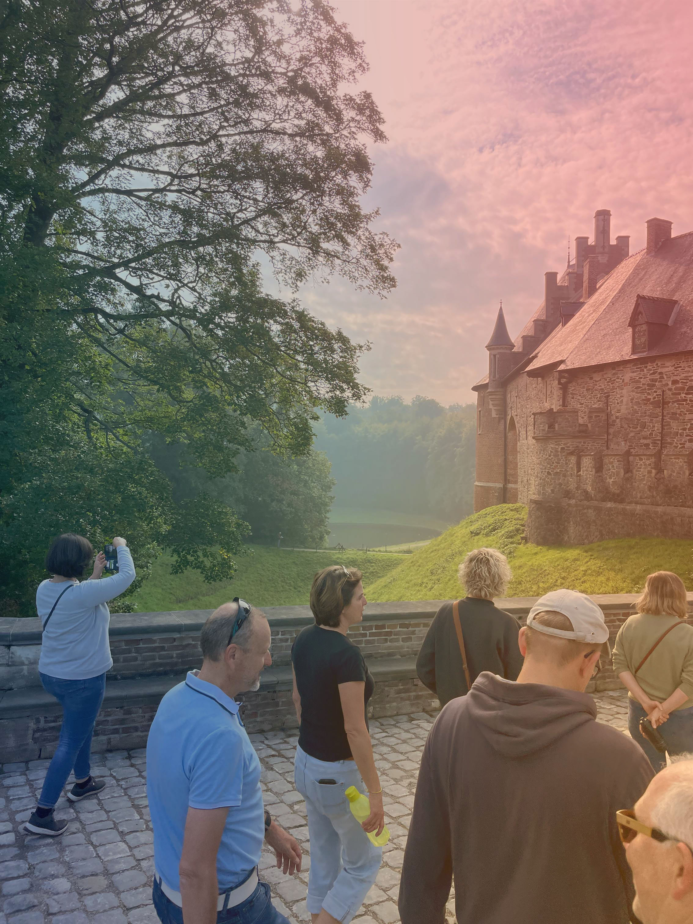 Groep mensen bij een middeleeuws kasteel omgeven door groen op een zonnige dag.