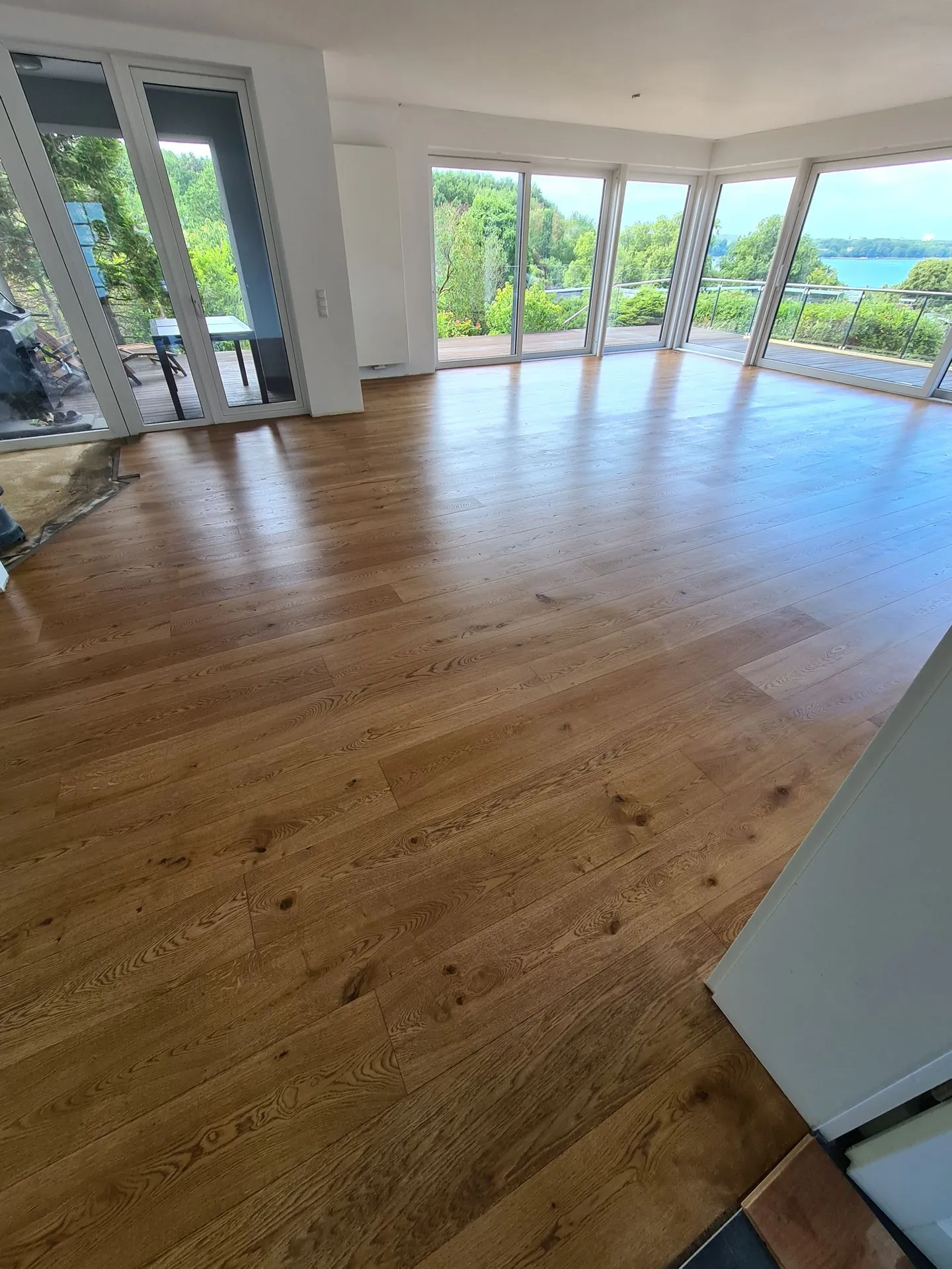 Leerer Raum mit Holzboden und Panoramafenstern mit Seeblick