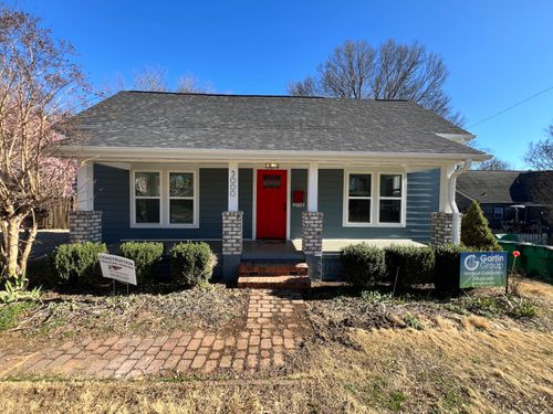 Single-story blue house with a red front door, brick steps, and bushes in front, under a clear blue sky.