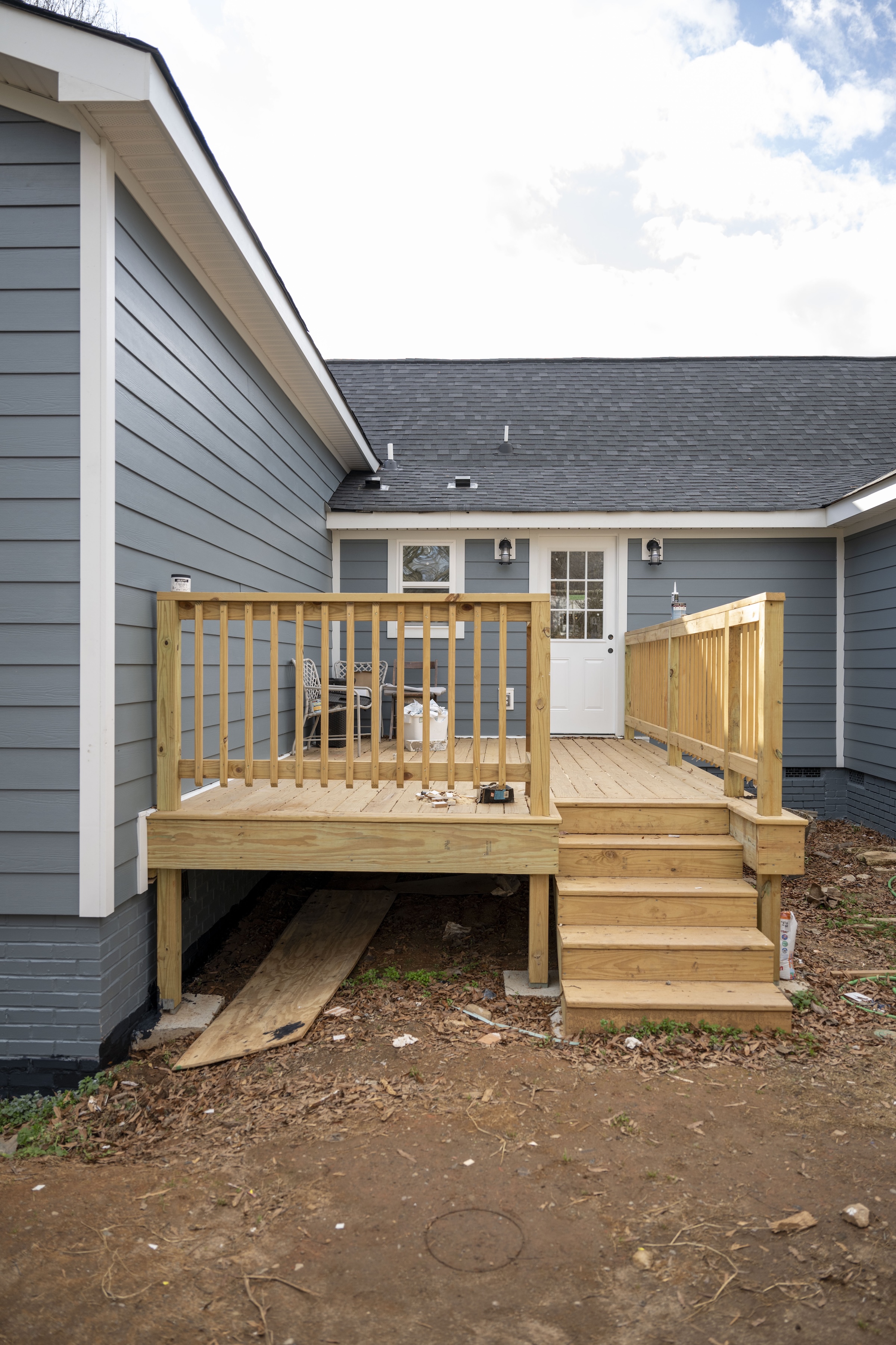 Side porch with new wooden decking, stairs, and railings attached to a blue house with a white door and window.