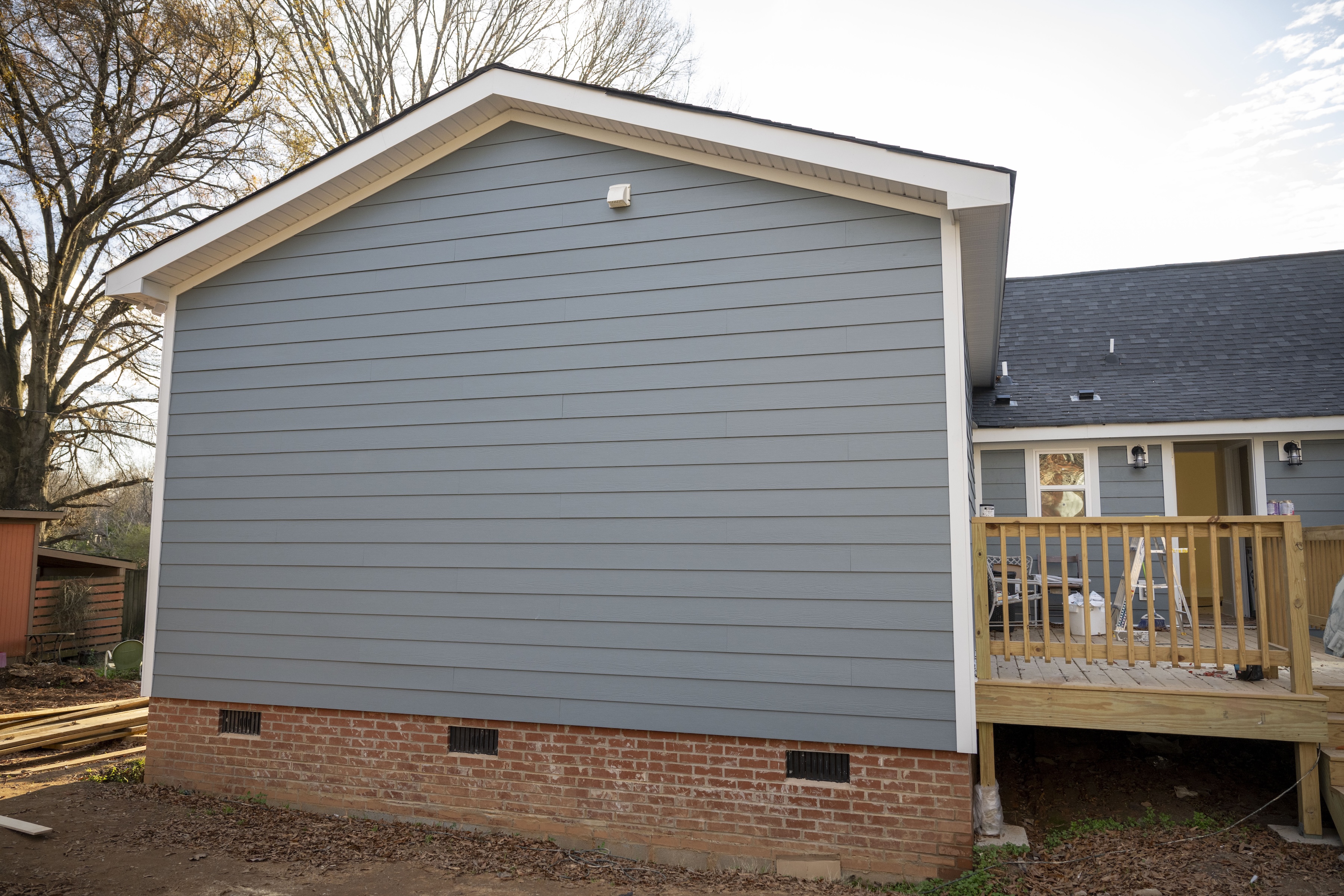 Side view of a house with blue siding, brick foundation, and a wooden deck under construction.