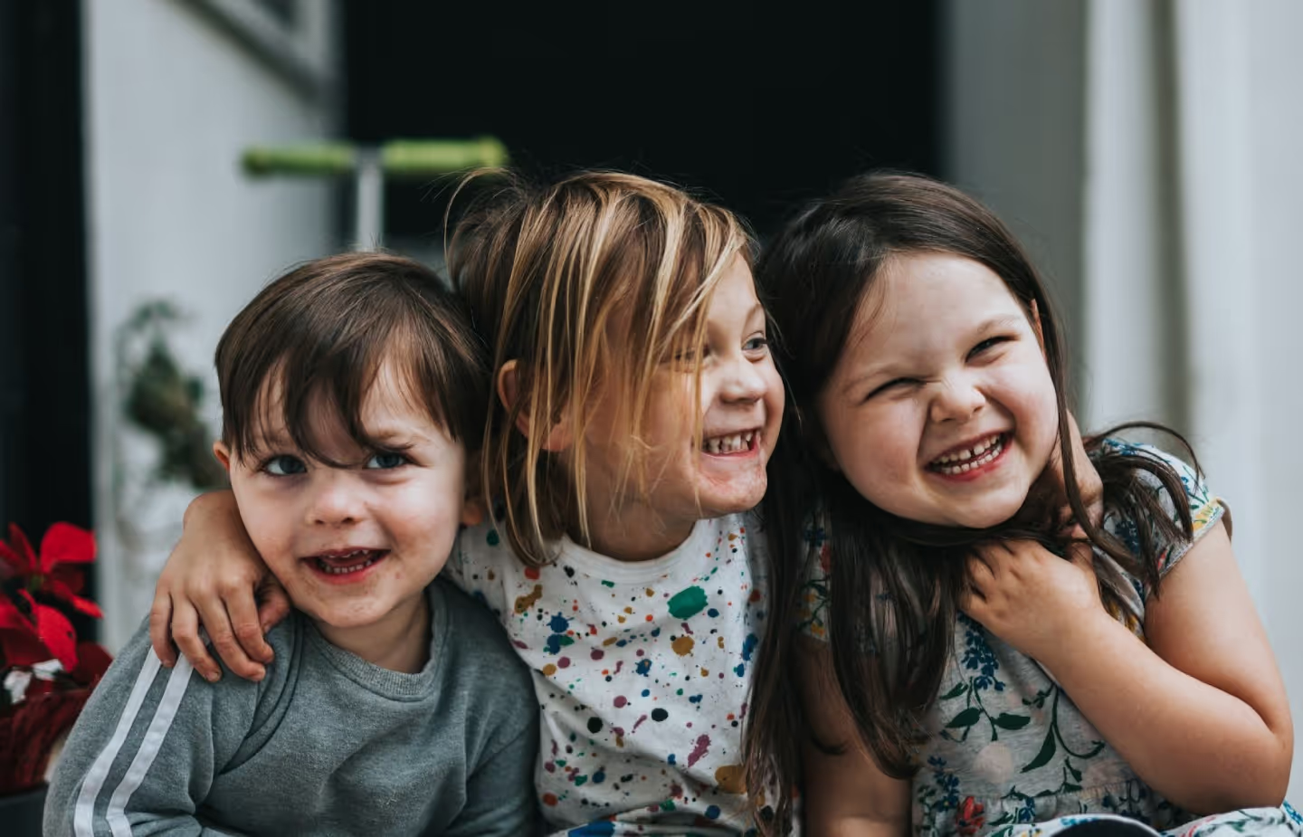 Three smiling children sitting closely together outdoors.